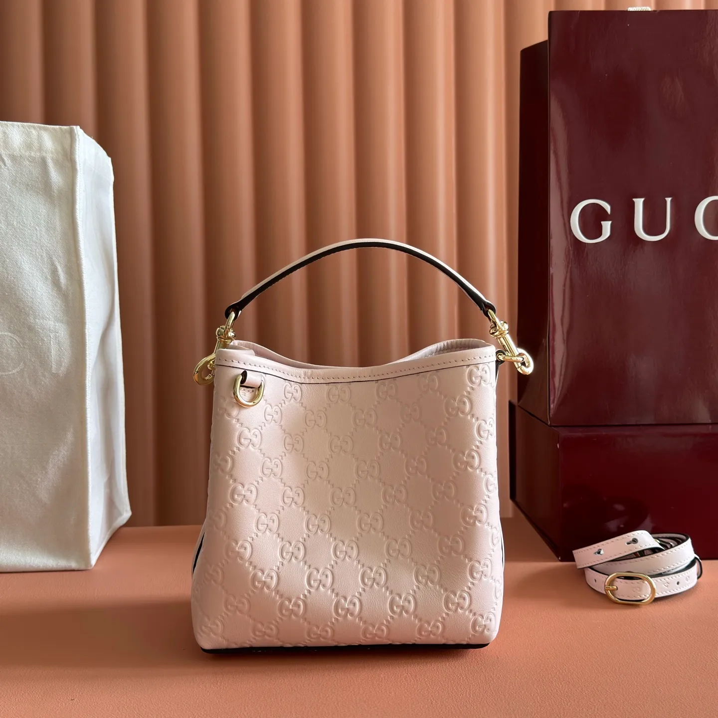 p1140. 💋💋💋【With full set of original counter packaging】GG Emblem series reinterprets the brand's timeless elegance and exquisite craftsmanship. Lined in webbed cotton, this bucket bag features an internal compartment for added functionality. Apricot pink GG printed embossed calf leather Light gold tone hardware Taupe cotton and linen lining Additional D-ring for attaching removable items Interior: two compartments and a central snap compartment Top handle with hook closure (height: 14 cm) Removable and adjustable calf leather shoulder strap (height: 52 cm - 57.5 cm; length: 107 cm - 114 cm) Magnetic snap closure Ident No.: 815118. Dimensions: 19cm (W) x 18cm (H) x 11cm (D) Weight: Approx. 0.45kg Color: Apricot Pink/Embossed. Made in Italy