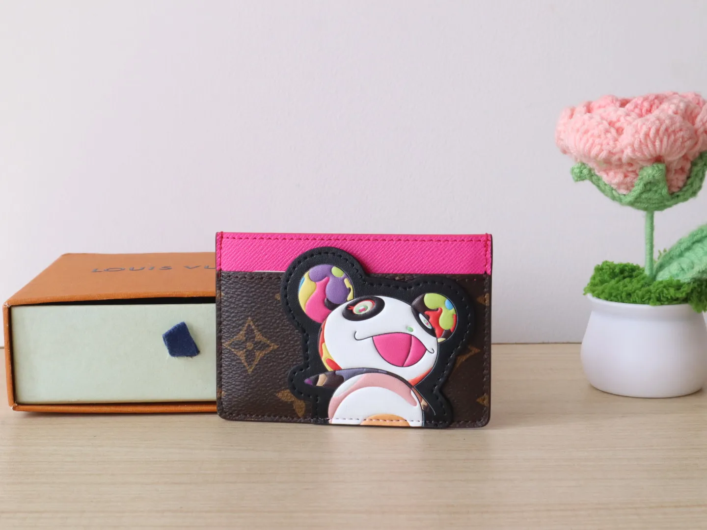 M13439 Card Holder🌟P280 LV x TM Business Card Holder This essential business card holder is reinterpreted with lively details from the Louis Vuitton x Murakami collaboration series, full of joy. The brand's classic Monogram pattern is covered with a bright panda pattern created by Japanese artists, which complements each other with a bright touch of pink on the top. Crafted from coated canvas, the business card holder has a stylish cut and multiple compartments to keep everyday essentials such as business cards and receipts organized.  11 x 7 x 0.5 cm
