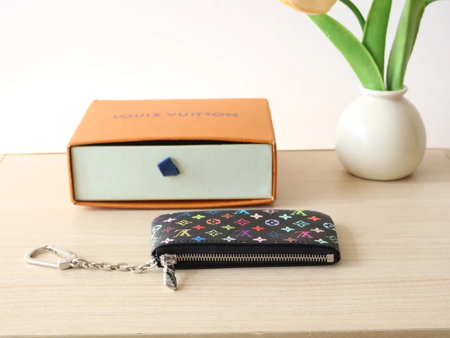 13664 Tricolor Coin Purse🌟P84 This replica Louis Vuitton x Murakami series key coin purse is colorful and made of coated canvas. The vibrant iconic Monogram pattern reinterprets the brand logo with the theme of Japanese artist Takashi Murakami in rainbow tones. The key coin purse has a silver zipper and is equipped with a chain strap and hook buckle to store keys securely. 12 x 7 x 1.5 cm (length x height x width)