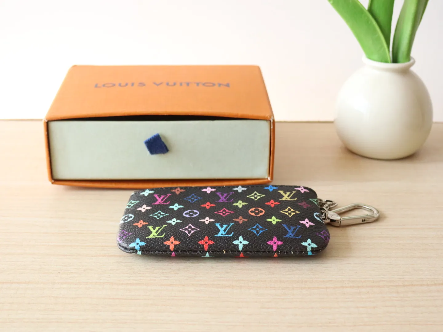 13664 Tricolor Coin Purse🌟P84 This replica Louis Vuitton x Murakami series key coin purse is colorful and made of coated canvas. The vibrant iconic Monogram pattern reinterprets the brand logo with the theme of Japanese artist Takashi Murakami in rainbow tones. The key coin purse has a silver zipper and is equipped with a chain strap and hook buckle to store keys securely. 12 x 7 x 1.5 cm (length x height x width)