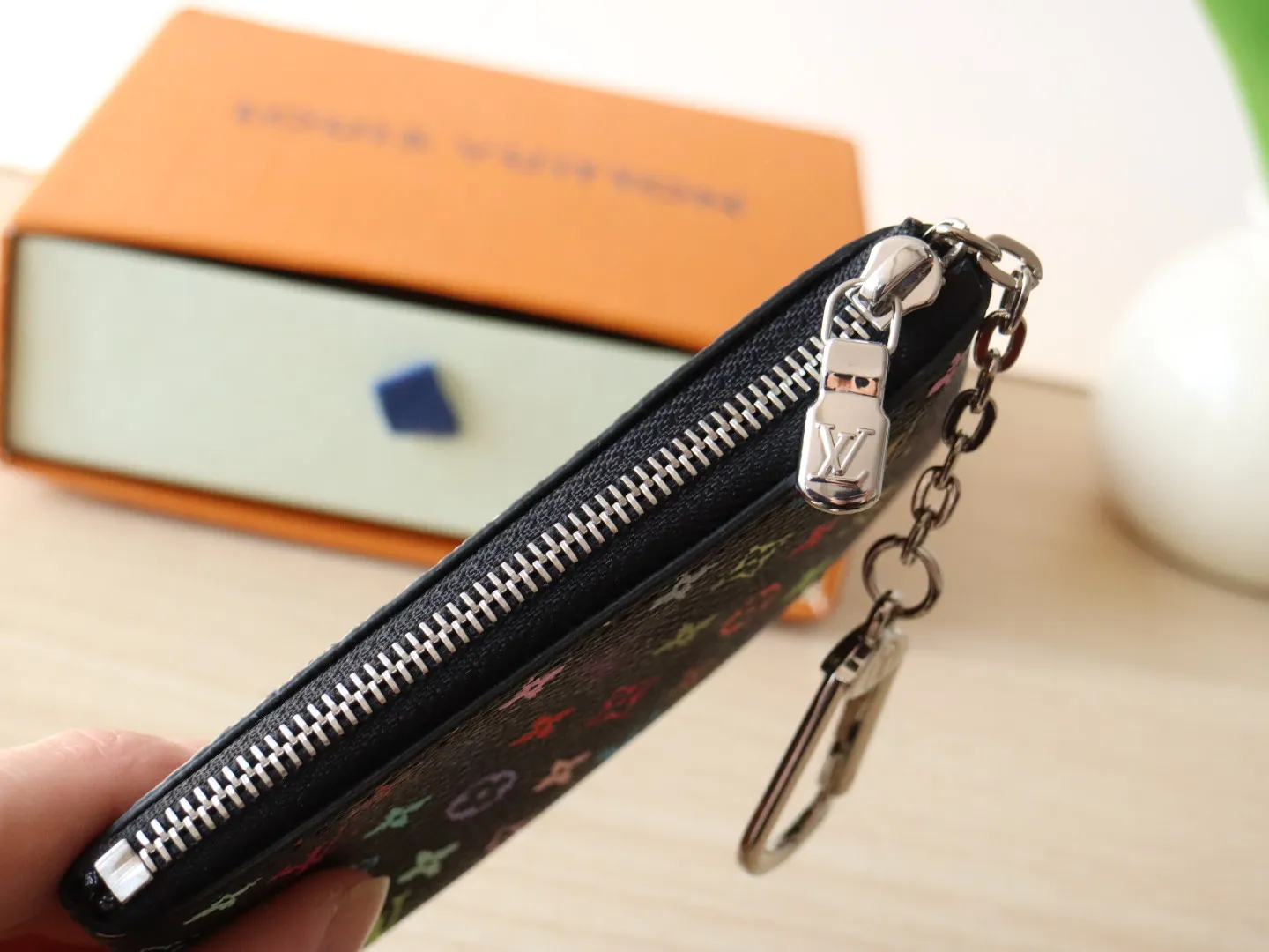 13664 Tricolor Coin Purse🌟P84 This replica Louis Vuitton x Murakami series key coin purse is colorful and made of coated canvas. The vibrant iconic Monogram pattern reinterprets the brand logo with the theme of Japanese artist Takashi Murakami in rainbow tones. The key coin purse has a silver zipper and is equipped with a chain strap and hook buckle to store keys securely. 12 x 7 x 1.5 cm (length x height x width)