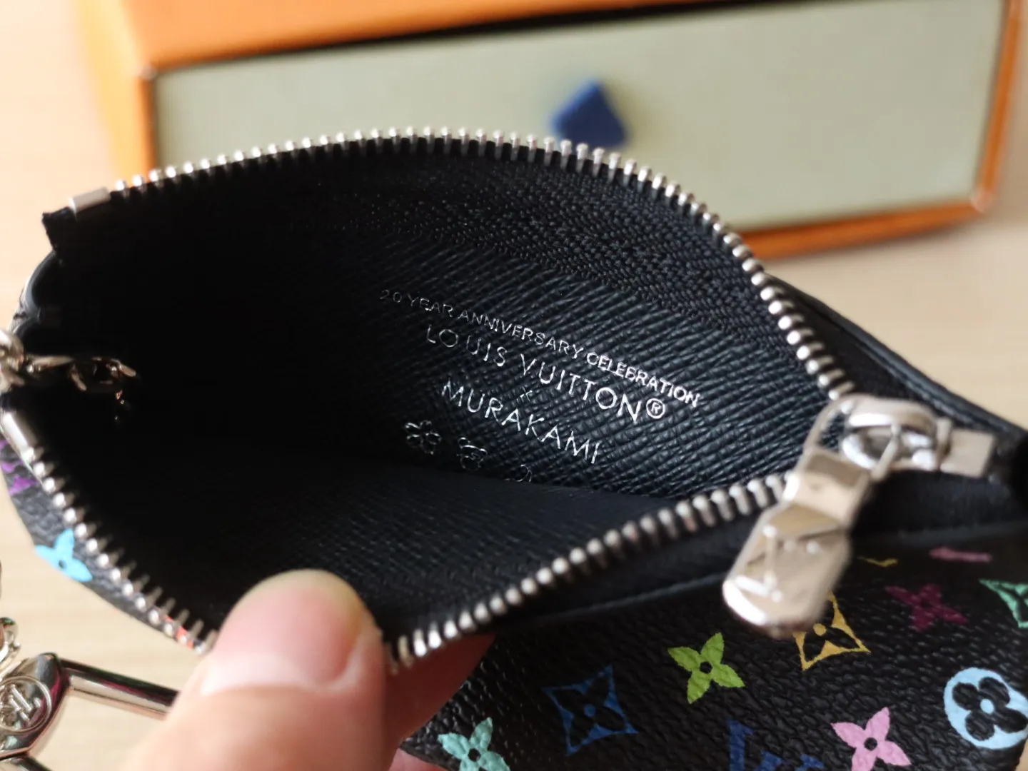 13664 Tricolor Coin Purse🌟P84 This replica Louis Vuitton x Murakami series key coin purse is colorful and made of coated canvas. The vibrant iconic Monogram pattern reinterprets the brand logo with the theme of Japanese artist Takashi Murakami in rainbow tones. The key coin purse has a silver zipper and is equipped with a chain strap and hook buckle to store keys securely. 12 x 7 x 1.5 cm (length x height x width)