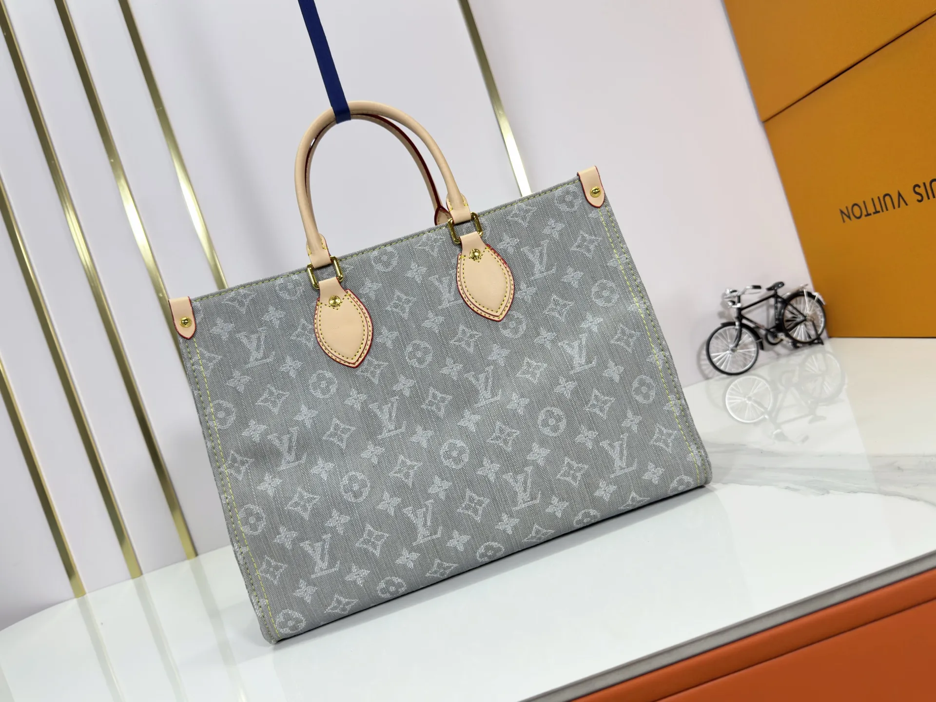 P320 M49495 M45659 M13189 New Gray Denim Denim This edition of OnTheGo MM celebrates the return of the iconic Monogram denim pattern in 2005. It's made from organic cotton, artfully woven with black and white threads and then bleached using a special Louis Vuitton technique to create a vintage-inspired finish. It's sized to hold a laptop, features light gold hardware, and includes signature details like natural leather accents and a removable name tag. Dimensions: 35 x 27 x 14 cm