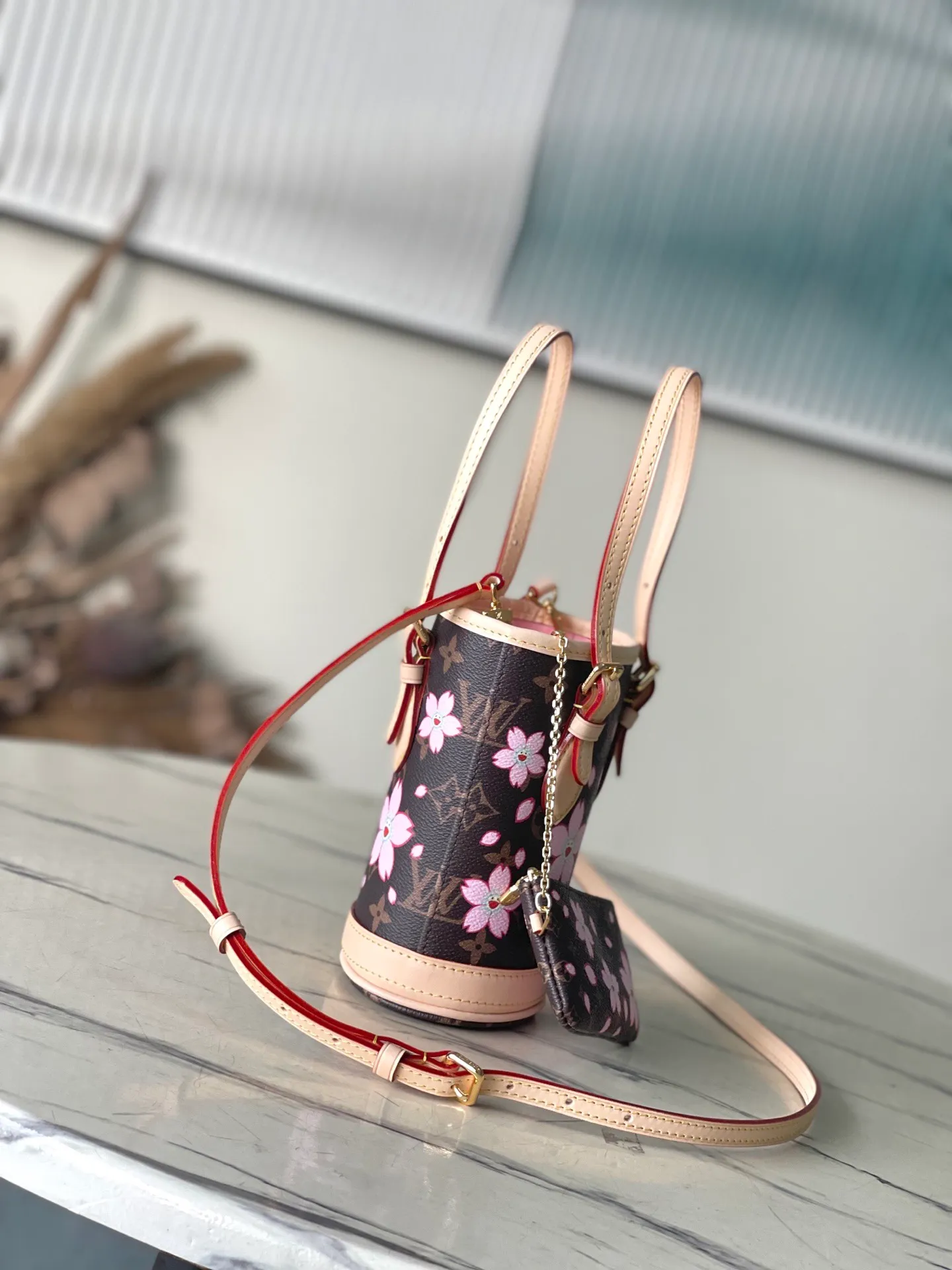 💰900 Top Original Order M13417 This Nano Bucket handbag is made of classic Monogram coated canvas and has a sophisticated design, with cow leather trim and dazzling metal parts to complete the whole. The Cherry Blossom pattern on the body of the bag conveys the atmosphere of prosperous recovery and highlights the distinctive style of Japanese artist Takashi Murakami. The detachable shoulder strap allows for a variety of carrying options, and the leather keychain adds a functional detail. Dimensions: 13 × 17 × 9 cm