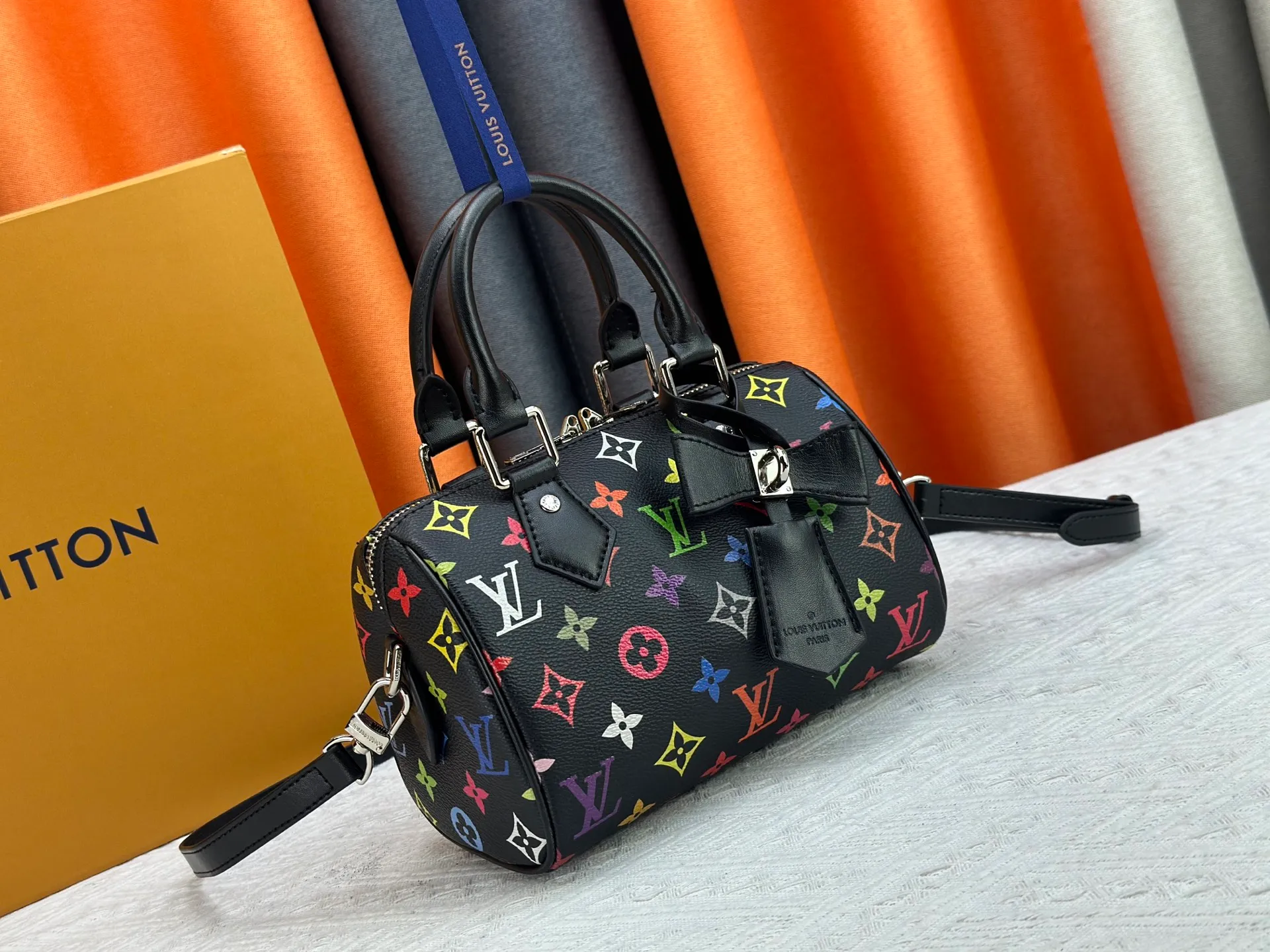 P260 Upgraded from the original version, this M46234 M46222 Speedy Bandoulière 20 handbag is made of soft coated canvas, with the full-length Monogram pattern traced in colorful rainbow tones, highlighting the smart style of the Louis Vuitton x Murakami reissue series. The Toron handle and detachable shoulder strap are constructed of cow leather, the metal corners recall classic luggage elements, and the bow-shaped key bag and padlock add brand touches. Dimensions: 20.5 x 13.5 x 12.0 cm (length x height x width)
