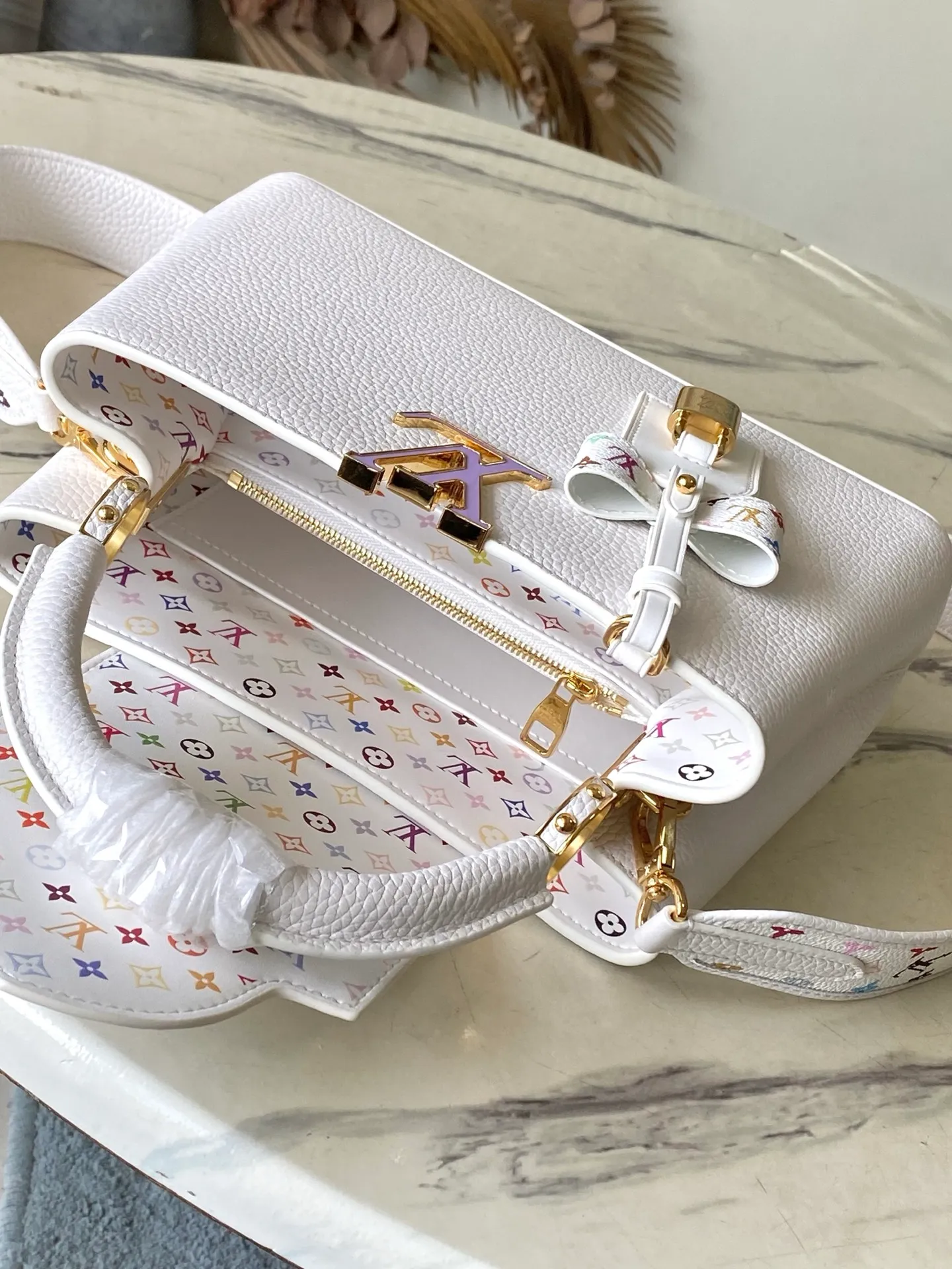 💰2360 "Special Original Leather" M13253 Small Size This Capucines handbag is from the Louis Vuitton x Murakami reissue series, using Taurillon cow leather to interpret the classic design. The LV letters and detachable Monogram strap are dipped in bright hues, a nod to the artist’s signature iridescent brushwork. The bow-shaped key holder and padlock decoration add sophisticated details, and the interior compartments and multiple pockets can easily store your daily needs. Dimensions: 27 × 17.3 × 9 cm