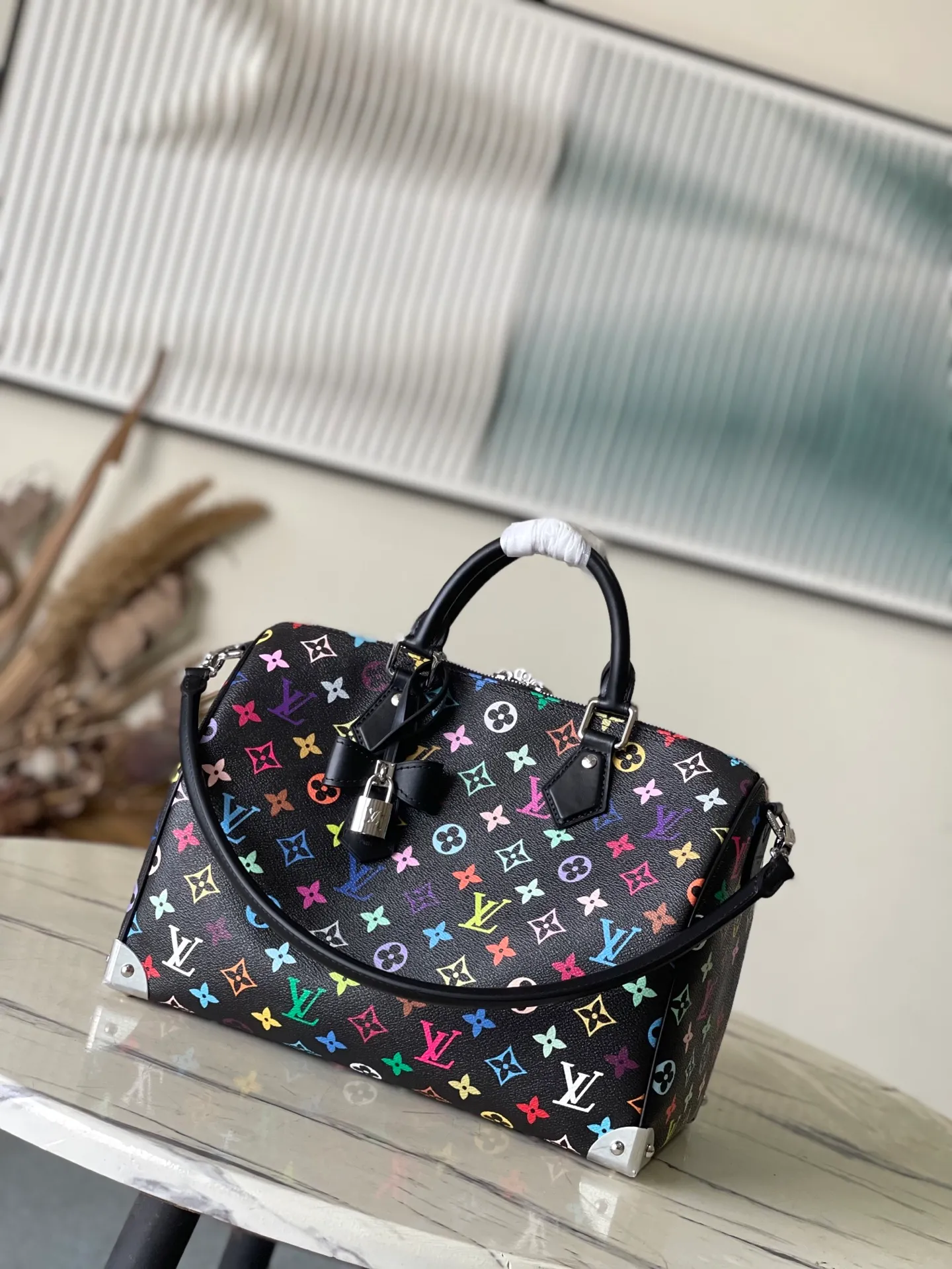 💰1180 Top Original M13257 This SpeedySoft 30 handbag is made of soft coated canvas, and the full-length Monogram pattern is traced in colorful rainbow tones, highlighting the smart style of the x Murakami Takashi reissue series. The Toron handle and detachable shoulder strap are constructed of cow leather, the metal corners recall classic luggage elements, and the bow-shaped key bag and padlock add brand touches. Dimensions: 30 × 21 × 17 cm