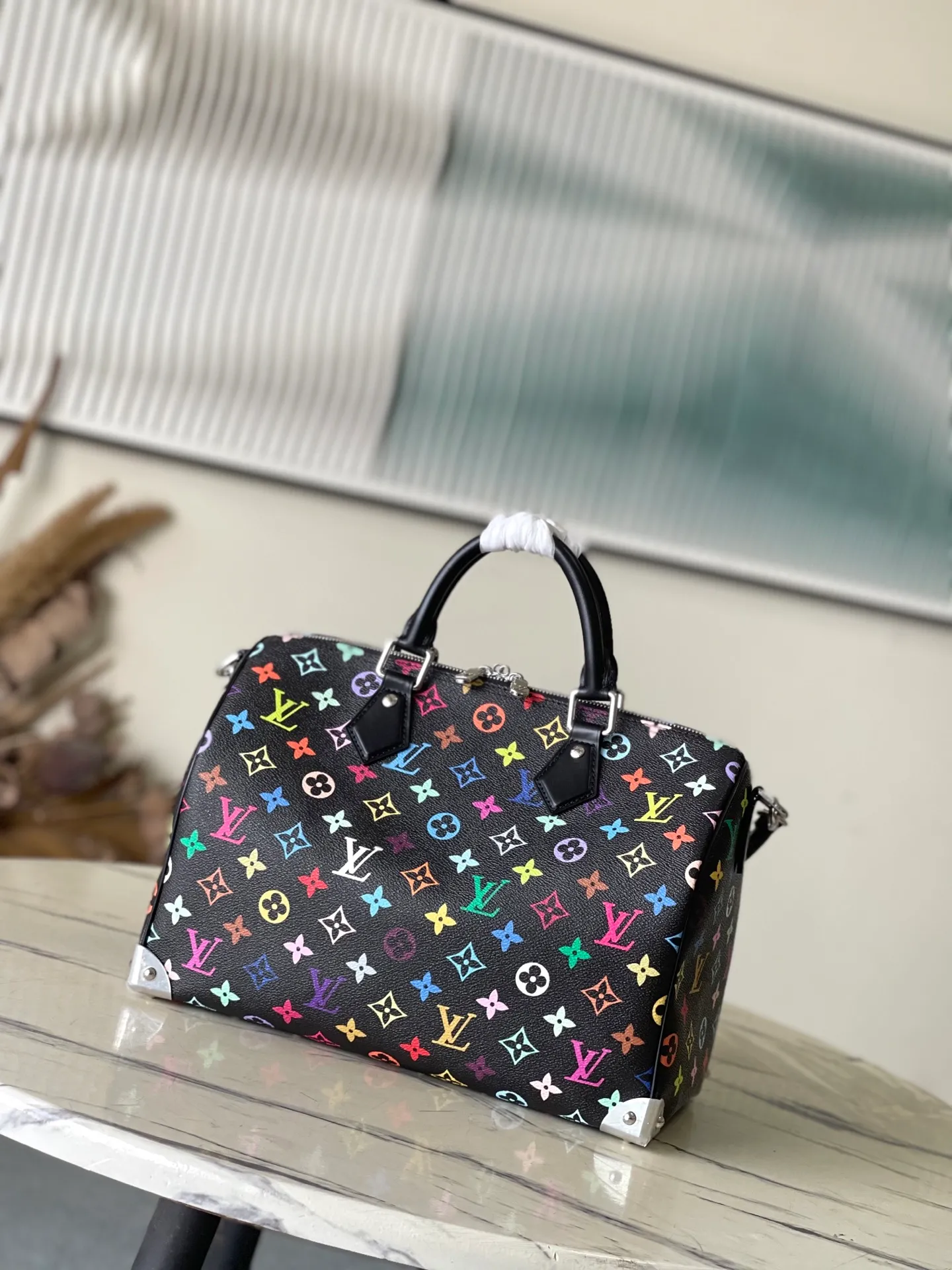 💰1180 Top Original M13257 This SpeedySoft 30 handbag is made of soft coated canvas, and the full-length Monogram pattern is traced in colorful rainbow tones, highlighting the smart style of the x Murakami Takashi reissue series. The Toron handle and detachable shoulder strap are constructed of cow leather, the metal corners recall classic luggage elements, and the bow-shaped key bag and padlock add brand touches. Dimensions: 30 × 21 × 17 cm