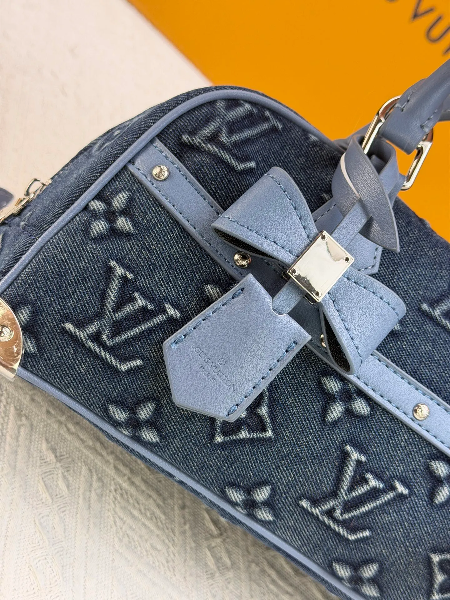 P360 M13084 Embossed Denim This Handbag East West handbag is from the Louis Vuitton x Takashi Murakami reissue series, using the artist's signature rainbow tones to trace the full-length Monogram pattern. Sleek horizontal construction lines the top handle, studded side straps, detachable and adjustable shoulder strap and LV x TM key holder, with cowhide leather details and sophisticated corners that nod to the brand's traditional luggage.  14 x 10 x 27 cm (H x W x L) Monogram coated canvas Cow leather trim Textile lining Metal hardware Zip closure Internal pocket Holds smartphone, keys, headphones and Zippy wallet Shoulder strap: removable, not adjustable Strap half-length: 44.0 cm Handle: Double handle