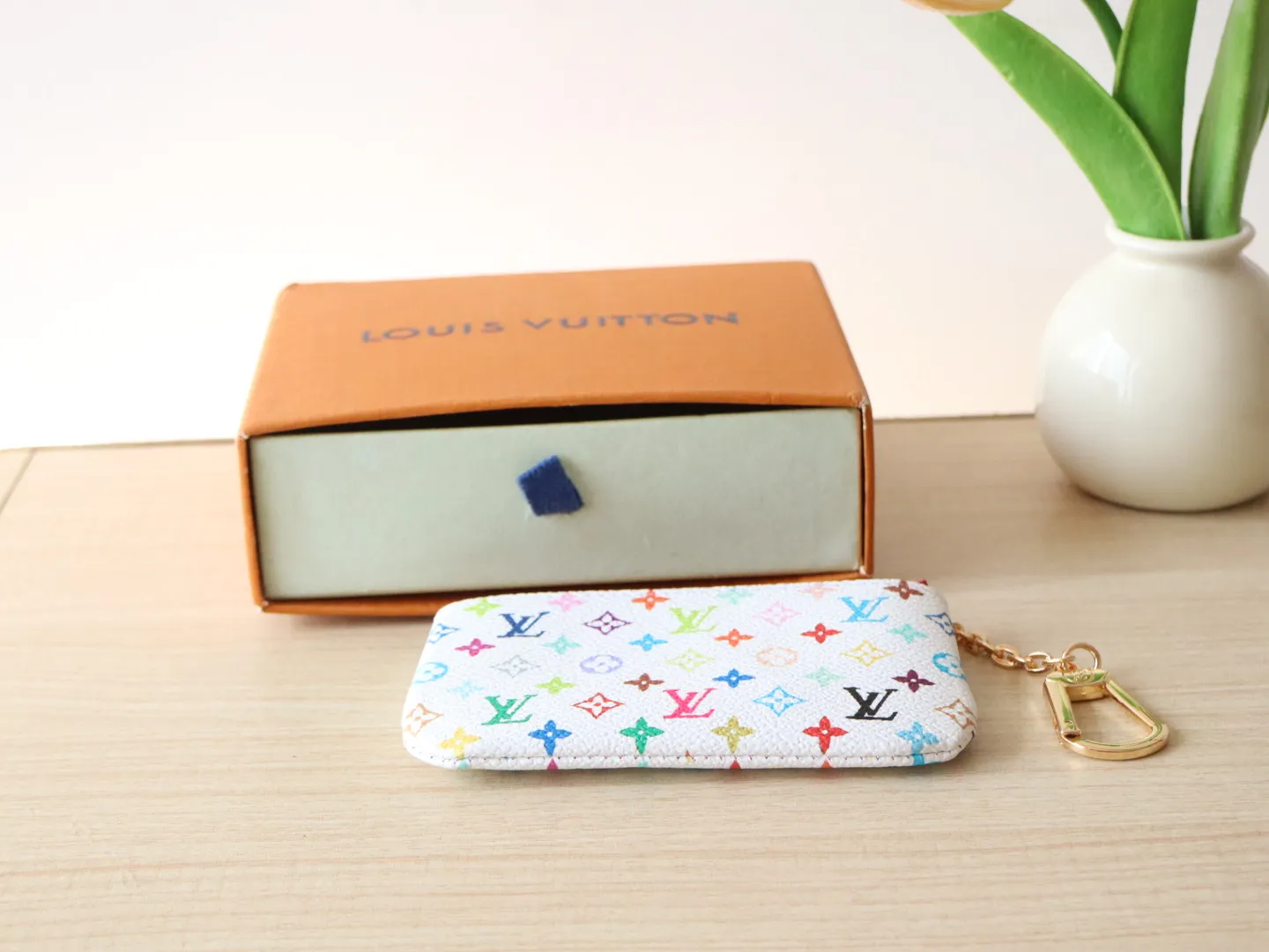 13664 Tricolor Coin Purse🌟P84 This replica Louis Vuitton x Murakami series key coin purse is colorful and made of coated canvas. The vibrant iconic Monogram pattern reinterprets the brand logo with the theme of Japanese artist Takashi Murakami in rainbow tones. The key coin purse has a silver zipper and is equipped with a chain strap and hook buckle to store keys securely. 12 x 7 x 1.5 cm (length x height x width)