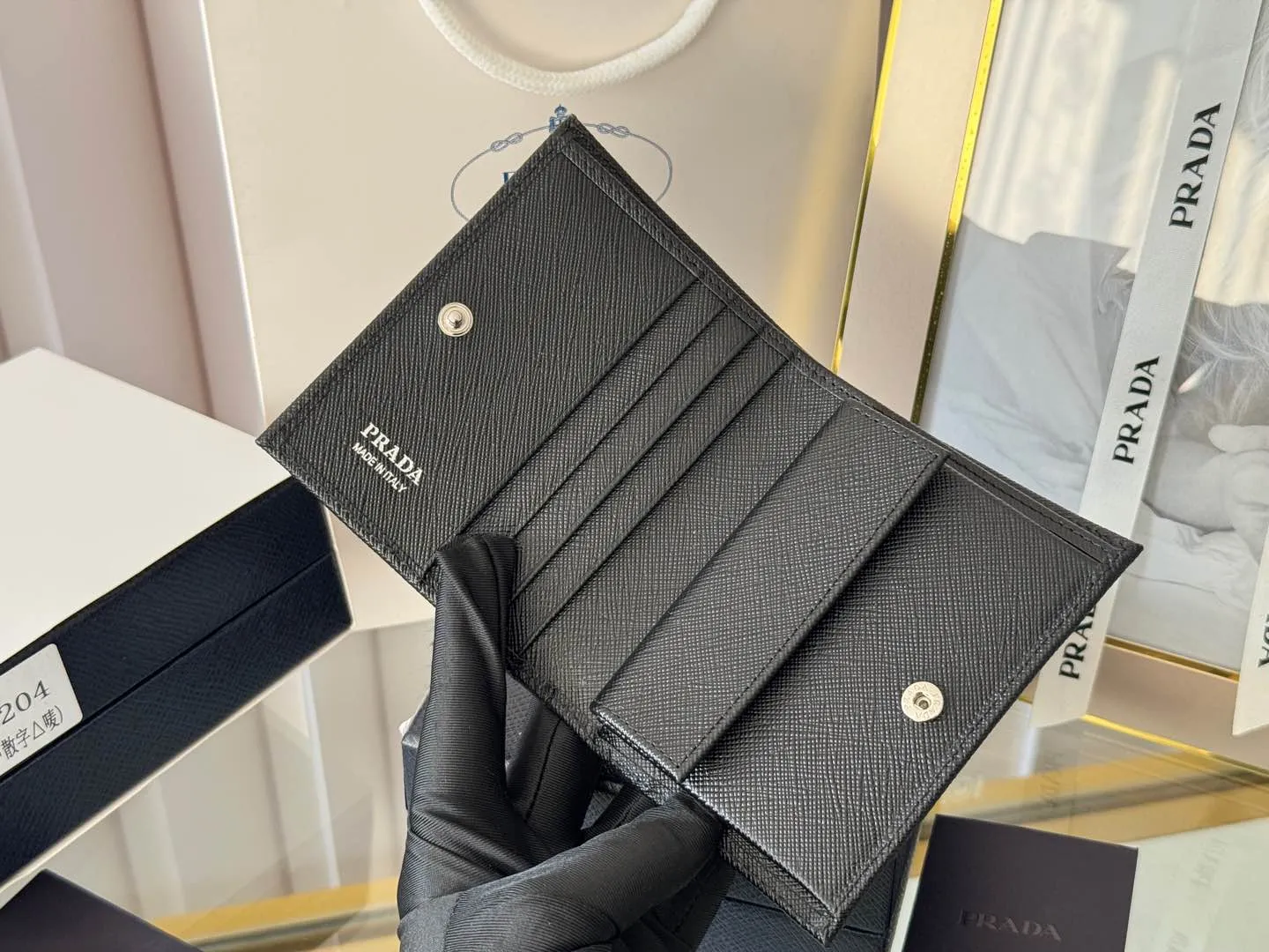 Prada women's two-fold short clip, with coin pocket and coin pocket. Model 1M0204, cross-grain cowhide. Size: 11.2x9.5cm. Simple and practical to enhance personal taste.
