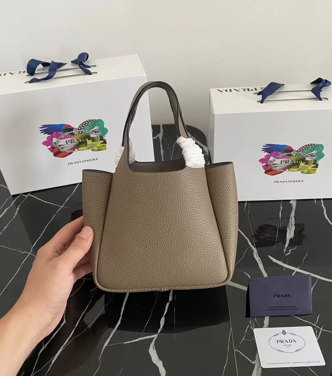 P1100¥ [Top original order] The latest 2022 vegetable basket tote bag mini model 1BA349 has arrived🎉🎉Soft and delicate pebbled calfskin tote bag, full leather inside and outside, equipped with double handles, decorated with silver metal logo, the overall body of the bag is very soft Lightweight, elegant and outstanding. The two side pockets not only meet the needs of exquisite storage but also add an elegant charm. It can be carried as a handbag or an armpit bag. It is a must-have handbag for fairies that perfectly combines classic heritage with the trend of the times. Size: 18︸15.5︸10CM!
