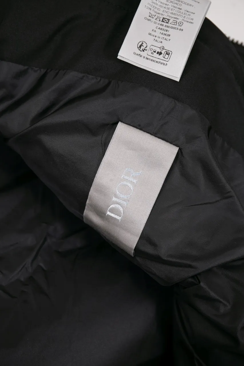 DIOR AND LEWIS HAMILTON JACKET Black technical fabric with removable sleeves This jacket is from the DIOR AND LEWIS HAMILTON limited series. Crafted from black technical fabric and embellished with DIOR AND LEWIS HAMILTON embroidery, the graphic design highlights the iconic Dior signature. With detachable sleeves, it can be worn in two different ways. It can be paired with jeans to create a low-key sporty look. DIOR AND LEWIS HAMILTON Embroidery and zip Knitted collar Detachable sleeves Front and internal flapless pockets Body: 100% nylon, Lining: 100% nylon