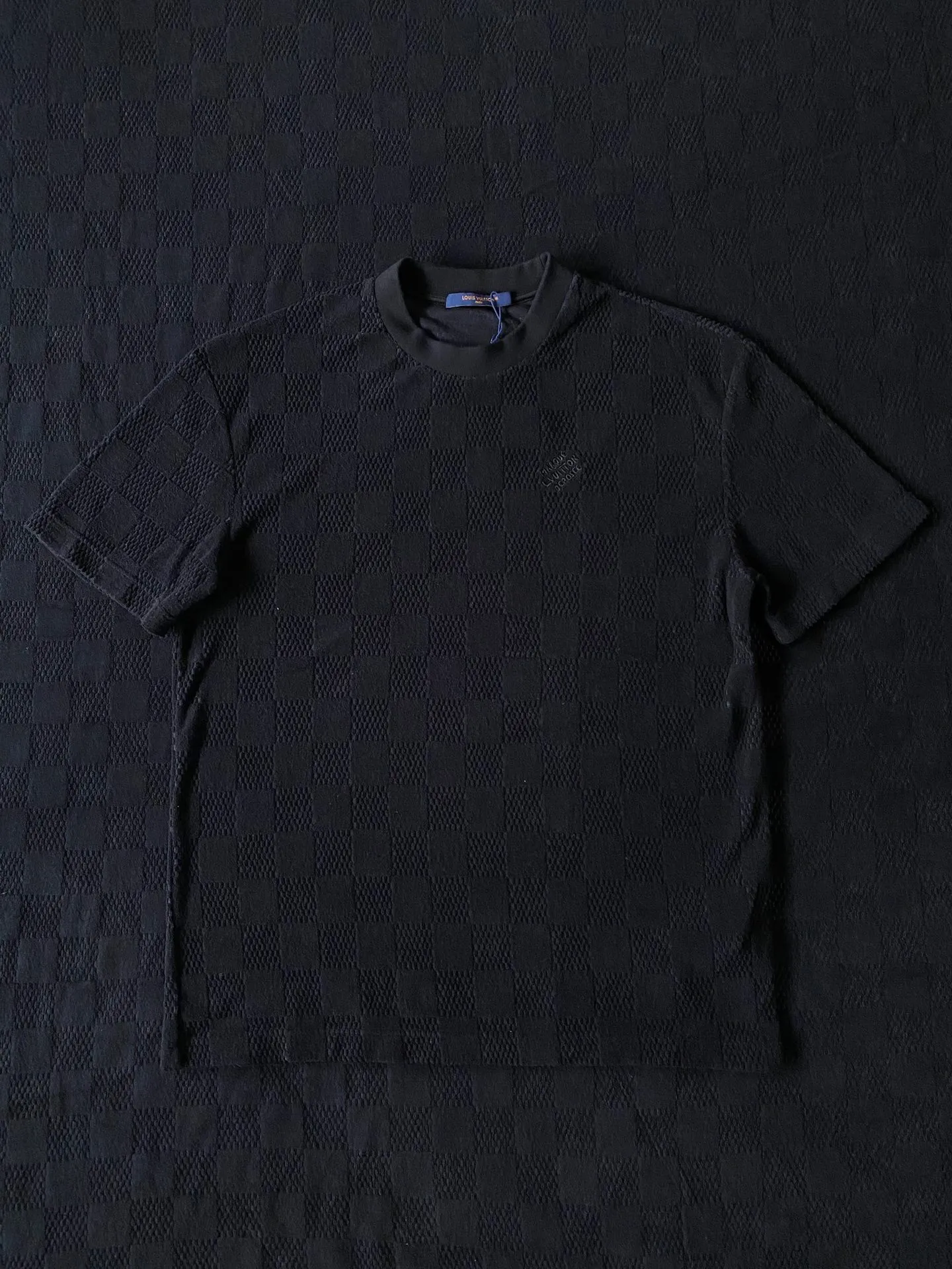 LV towel plaid round neck short sleeves ⚠️Original purchase, 650, standard fit, Damier terry cloth, embroidered Marque L.Uuitton deposee logo on the chest, ribbed collar, floral stitching, full set of accessories with #Damier terry cloth Towel jacquard fabric terry cloth is a fabric that looks like a towel. It has the advantages of high water absorption, good warmth retention, soft hand feel, stiff fabric, and not easy to deform, so it is called terry cloth.  During the weaving process of the full-width embossed pattern, computer digital programming is used to make the plate. The jacquard part has a concave and convex feel, the fabric has a soft and waxy feel, and the fabric details are delicate. The thermal conductivity of towel fabric is low, and because the cotton fiber itself is porous and elastic, a large amount of air can accumulate between the fibers, so the towel fabric has good moisture retention.  #Chest Marque L Uuitton deposee embroidery The chest is embellished with simple letter patterns, and the letter size spacing effect is consistent. Using linen embroidery thread combined with encrypted processing, the embroidery body has a subtle matte visual texture; the embroidery effect is three-dimensional and full. The smaller the embroidery, the more sophisticated and demanding it is. The embroidery thread is made of imported material, which is more flexible and glossy than ordinary embroidery thread; the stitches are clear and smooth, and have a three-dimensional texture effect.  #Positioning Pattern Cutting and Sewing The whole piece positioning pattern sewing process is a fine and complex technology. During the cutting process, it is necessary to ensure that the pattern or texture of each piece can perfectly match other pieces. Through floral tailoring, the checkerboard pattern of ready-made garments appears neatly arranged.  #straight round neck version. Cut and sewed in floral position, standard H hanging version, with shoulder-length design. The vertical version emphasizes that the width of the shoulders, waist, and hem are basically the same, and it is simple and loose. The short sleeves are tailored to fit the body of the wearer. At the same time, the neckline, cuffs and hem of the short sleeves are all designed with double lines.
