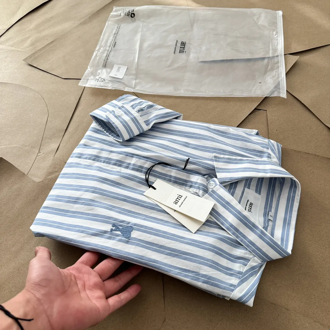 Ami Paris Oxford cotton button-down corner collar casual shirt-blue heart thick striped long-sleeved shirt-same style for men and women. Blue small love letter embroidery decoration fashionable and versatile long-sleeved shirt! On sale simultaneously at counters!  A well-known French affordable luxury fashion brand. The brand's classic elements are embellishments sought after by major celebrities. Its basic simple design and fashionable style make it a must-have couple's shirt for men and women!  Made of custom-woven 100% Oxford cloth pure cotton, it feels soft and delicate, has excellent moisture absorption and perspiration performance, and is very comfortable and skin-friendly when worn next to the skin! The chest of the shirt is decorated with the classic love letter A logo embroidery. The top-notch embroidery technology is tight, full and full of details, and is cleverly embellished with bright red. It carries all the eye-catching points. It follows the consistent minimalist French attitude. The fabric is soft and comfortable, suitable for any versatile casual shirt couple!  Color: Blue Stripe Size: S-XL S: Bust 106 Shoulder Width 47 Clothing Length 71 Sleeve Length 60 M: Bust 110 Shoulder Width 48 Clothing Length 73 Sleeve Length 61 L: Bust 114 Shoulder Width 49 Clothing Length 75 Sleeve Length 62