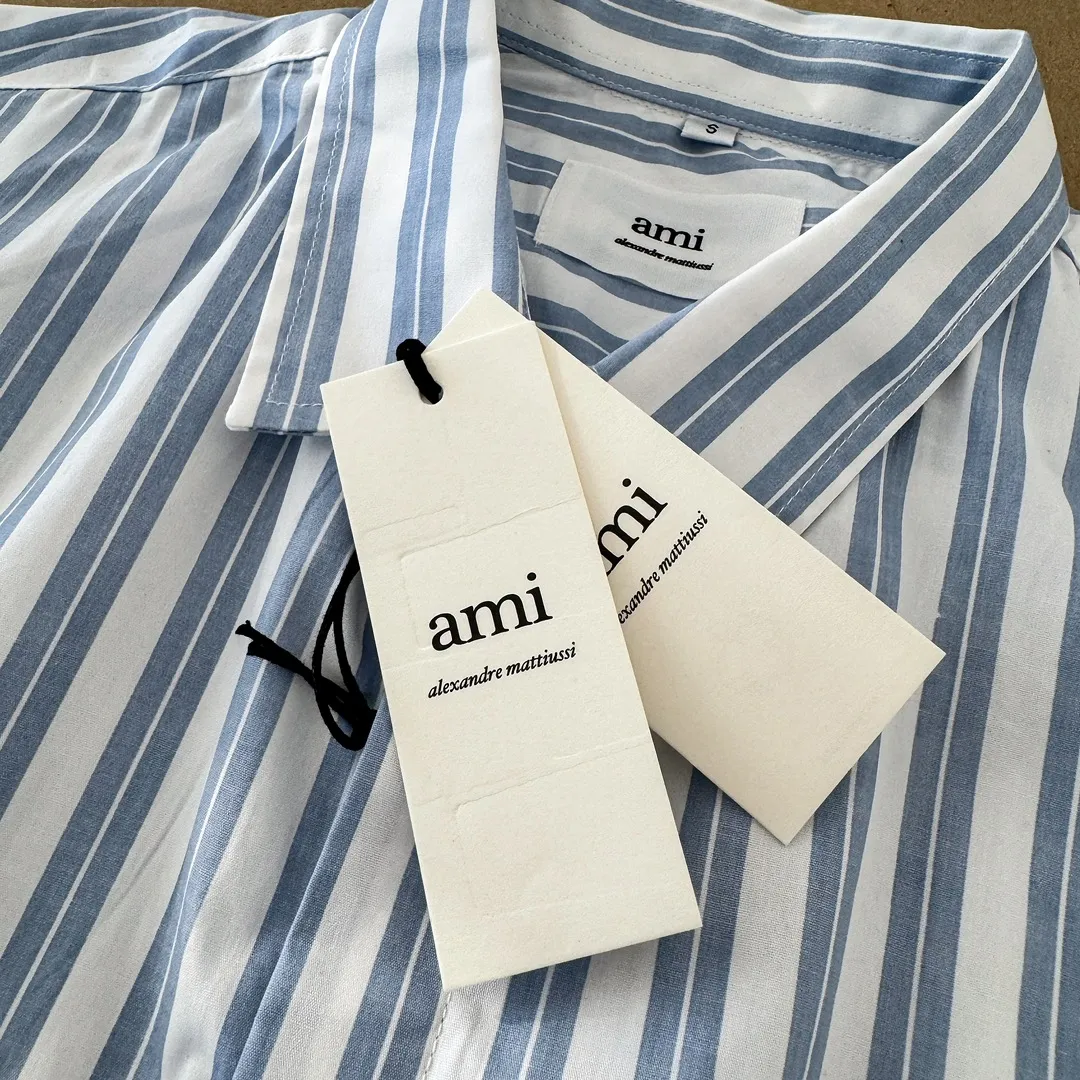 Ami Paris Oxford cotton button-down corner collar casual shirt-blue heart thick striped long-sleeved shirt-same style for men and women. Blue small love letter embroidery decoration fashionable and versatile long-sleeved shirt! On sale simultaneously at counters!  A well-known French affordable luxury fashion brand. The brand's classic elements are embellishments sought after by major celebrities. Its basic simple design and fashionable style make it a must-have couple's shirt for men and women!  Made of custom-woven 100% Oxford cloth pure cotton, it feels soft and delicate, has excellent moisture absorption and perspiration performance, and is very comfortable and skin-friendly when worn next to the skin! The chest of the shirt is decorated with the classic love letter A logo embroidery. The top-notch embroidery technology is tight, full and full of details, and is cleverly embellished with bright red. It carries all the eye-catching points. It follows the consistent minimalist French attitude. The fabric is soft and comfortable, suitable for any versatile casual shirt couple!  Color: Blue Stripe Size: S-XL S: Bust 106 Shoulder Width 47 Clothing Length 71 Sleeve Length 60 M: Bust 110 Shoulder Width 48 Clothing Length 73 Sleeve Length 61 L: Bust 114 Shoulder Width 49 Clothing Length 75 Sleeve Length 62