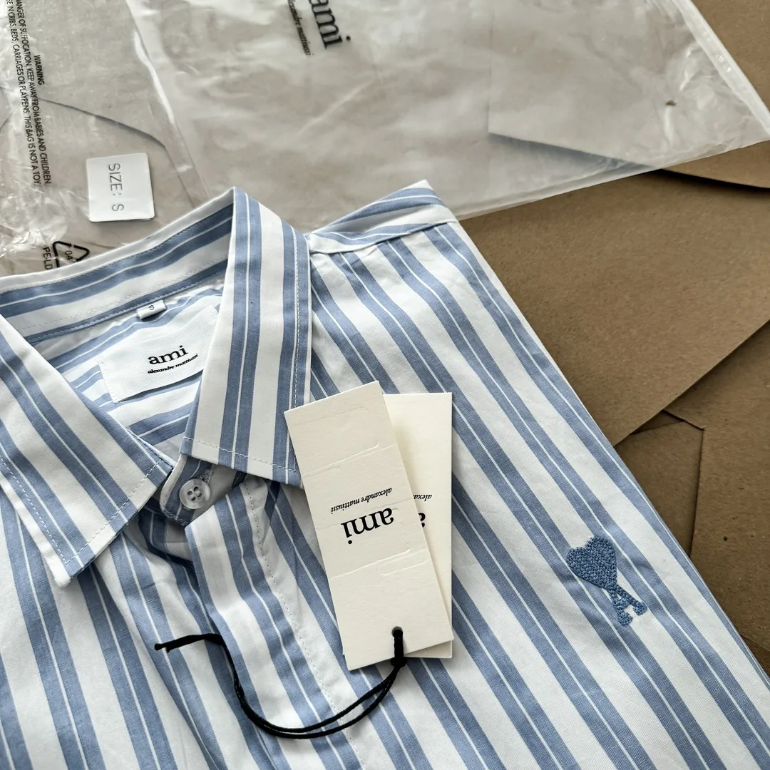 Ami Paris Oxford cotton button-down corner collar casual shirt-blue heart thick striped long-sleeved shirt-same style for men and women. Blue small love letter embroidery decoration fashionable and versatile long-sleeved shirt! On sale simultaneously at counters!  A well-known French affordable luxury fashion brand. The brand's classic elements are embellishments sought after by major celebrities. Its basic simple design and fashionable style make it a must-have couple's shirt for men and women!  Made of custom-woven 100% Oxford cloth pure cotton, it feels soft and delicate, has excellent moisture absorption and perspiration performance, and is very comfortable and skin-friendly when worn next to the skin! The chest of the shirt is decorated with the classic love letter A logo embroidery. The top-notch embroidery technology is tight, full and full of details, and is cleverly embellished with bright red. It carries all the eye-catching points. It follows the consistent minimalist French attitude. The fabric is soft and comfortable, suitable for any versatile casual shirt couple!  Color: Blue Stripe Size: S-XL S: Bust 106 Shoulder Width 47 Clothing Length 71 Sleeve Length 60 M: Bust 110 Shoulder Width 48 Clothing Length 73 Sleeve Length 61 L: Bust 114 Shoulder Width 49 Clothing Length 75 Sleeve Length 62