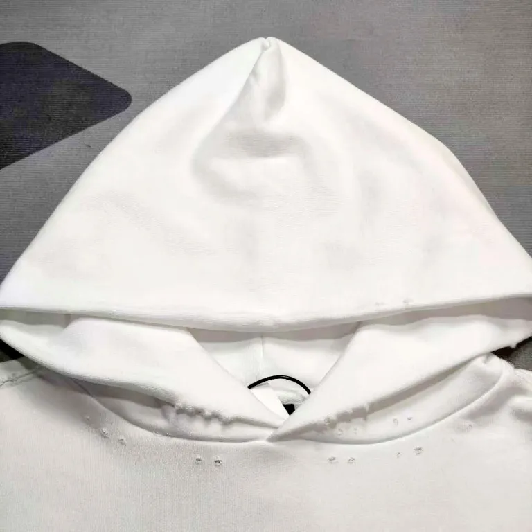 The top proven version of Balenciaga 23SS masking paper printed letters double-sided logo hooded loose hooded sweatshirt. This hoodie has a very interesting and cute design. The kangaroo pocket on the front of the large body is reverse-cut design. The double side pockets are hollow, which means that when viewed from the front, it actually deceives your vision. The real pockets are sewn on the reverse terry bottom. It is time-consuming and labor-intensive, but it is the core theme of the entire hoodie that cannot be ignored. The same detail is that the double side pockets are hemmed and stitched. And processed with holes; 480g heavy-weight pure cotton fabric with fine small terry bottom. After heavy mud dyeing and washing, the fabric still has a thick foundation and is comfortable and soft. The front and back double-sided textured paper transfer LOGO, and the front and back printing colors are different. The loose and large drop shoulder design is unisex. This style is also very suitable for girls to match. It is easy to create a lazy and casual street feel of the United States and France. Many holes are processed by hand grinding wheels on the body. Traces of muddying can be seen on the neckline, shoulder line, and side cuff splicing, but the visual effect transition is natural and soft without any sense of dirt. The old effect of the entire hoodie is excellent. The cuff threads are custom-woven in color; the packaging is washed and customized. The new gray silver letter main logo. The dropped shoulder model does not include shoulder width. The version is Kanye’s American style. Short and wide street casual version. From short sleeves to sweaters, this style is definitely not to be missed. Color: mud-dyed custom-woven navy Size: XS-S-M (Can be worn by both men and women, OS is loose and dropped on the shoulders) P:510
