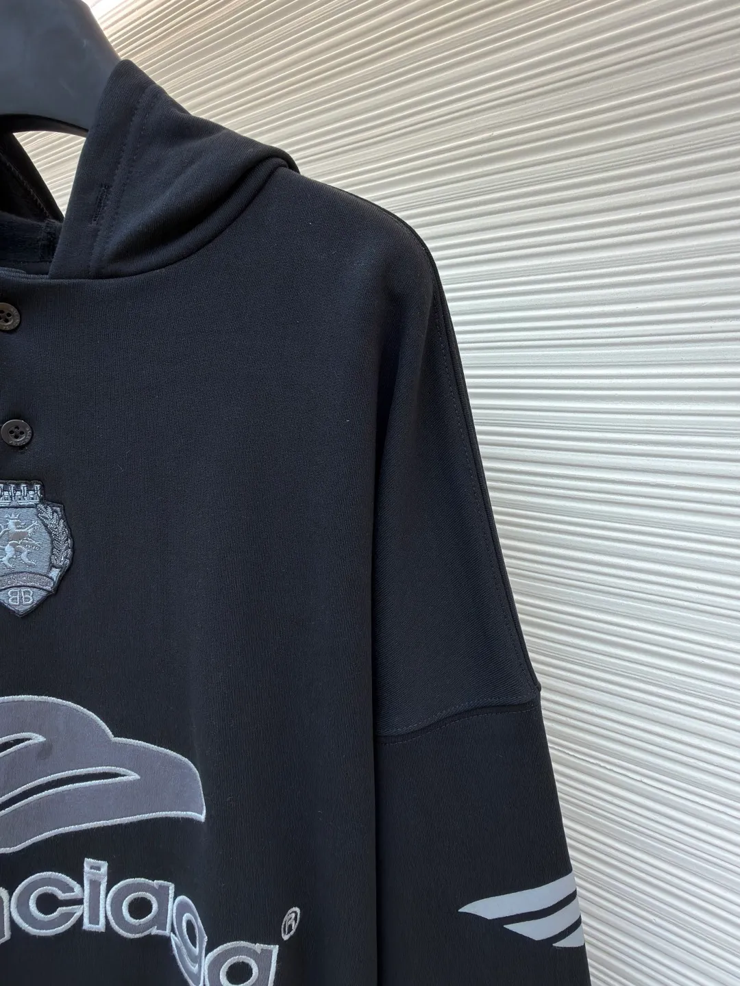 Balenciaga 3B football Polo hoodie ●Original version: Purchased and developed for 9999 ●Item number: 1681997-B40 ●Fabric: cotton fabric ●Technology: embroidery applique production ●Color: black ●Version: loose fit ●Weight: about 860 grams ●Size: XS-S-M-L ●Description: The neckline adopts a half-open button design and is decorated with metal badges to enhance the layered look; the main body of the garment presents the brand logo through three-dimensional foam printing technology, and the grayscale gradient effect enhances the visual texture. The cuffs and hem are edged with contrasting ribbing, which has moderate elasticity and is not easily deformed; a collage label is embedded in the left hem, and the details echo the brand's street style. The partial logo embroidery on the shoulders and cuffs echoes the main pattern. The overall craftsmanship takes into account practical wearability and brand recognition, making it suitable for daily casual or trendy looks. The overall wiring is straight and delicate, the fabric is comfortable and soft, and the color is consistent without color difference. It can be matched with the same style to create a fashionable look and control various occasions. Customized accessories, complete with three standards, same style for men and women!