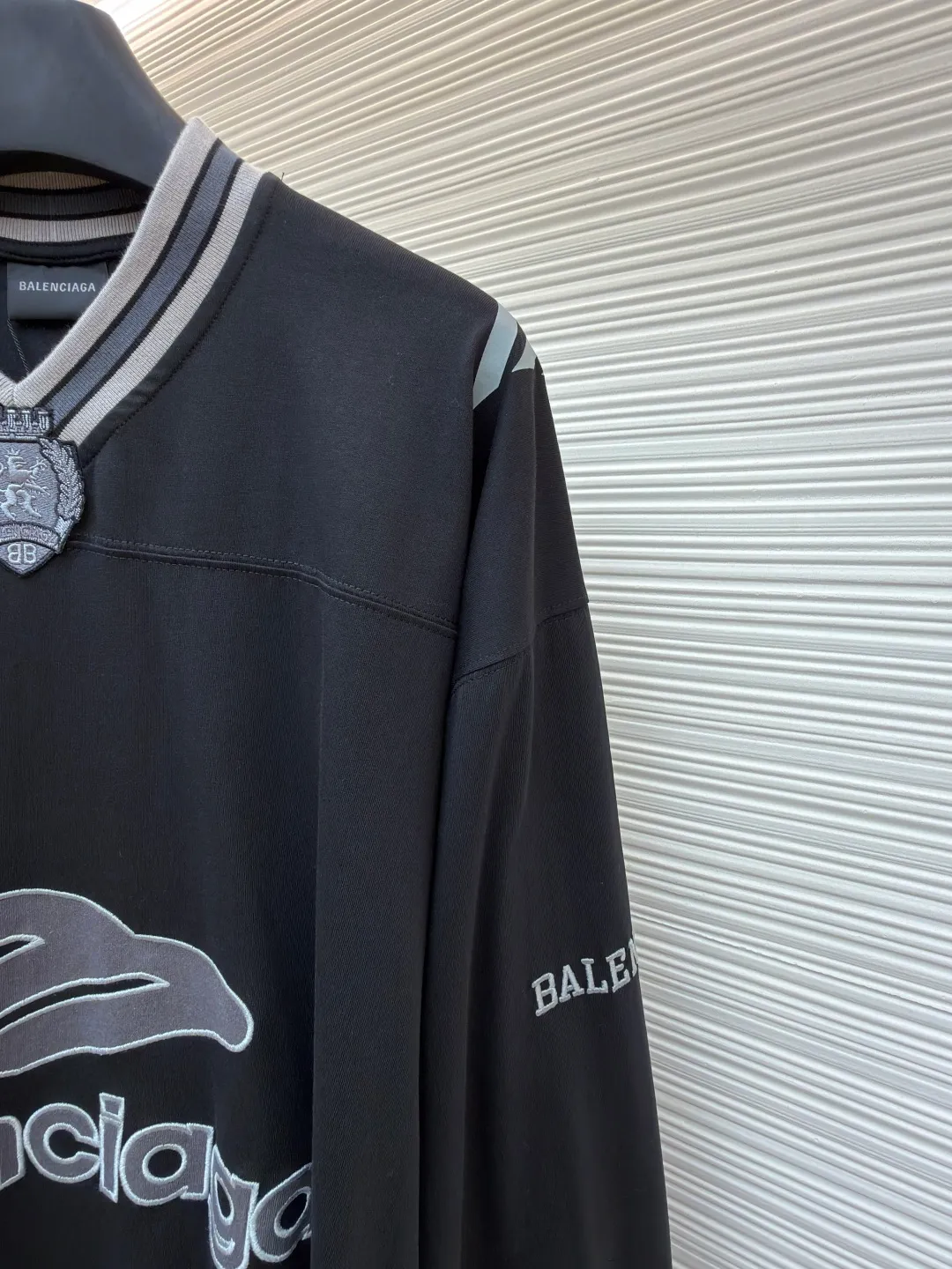 Balenciaga team series V-neck long sleeves ●Original version: purchased and developed by 8016 ●Item number: 1682073-A55 ●Fabric: plain knitted compact cotton fabric ●Technology: glue printing ●Color: black ●Version: loose version ●Weight: about 380 grams ●Size: XS-S-M-L ●Description: The main body is made of 24-count special woven compact cotton, with a weight of 185g/㎡. Compact spinning technology is applied in the spinning process, which significantly reduces yarn hairiness and makes the yarn smoother and stronger. This gives the fabric an unusually dense structure, a smooth and smooth surface, and excellent pilling resistance, while retaining the softness and breathability of pure cotton. The weight of 185g is light to middleweight, ensuring that the clothing is light, drapeable and can move freely. It is very suitable for creating a long-sleeved shirt that combines sportiness with daily comfort. The V-neck part is made of two different colors of high-elastic rib fabrics. The process step is to first weave ribbed belts of two colors separately, and then through precise cutting and splicing, form a V-shaped neckline with sharp color contrast. It breaks the monotony of the solid color body, uses strong color contrast to create a young and energetic visual focus, and optimizes the neck line. The pattern is pre-cut and formed into patches on fabrics of different materials or colors, and then covered on the body. Finally, high-density embroidery thread is used to fix the edges and outline the internal details. Its function is to create patterns with bright colors, strong texture contrast, three-dimensionality and durability. The edges of the pattern are strong and not easy to wear. A special elastic paste is screen-printed on the sleeves to create brightly colored patterns with a slightly coated feel. The elastic paste ensures that the printed area can stretch with the fabric without cracking. It forms a texture contrast between one flat and one convex with the three-dimensional sense of appliqué, which increases the interest and complexity of the design. The overall wiring is straight and delicate, the fabric is comfortable and soft, and the color is consistent without color difference. It can be matched with the same style to create a fashionable look and control various occasions. Customized accessories, complete with three standards, same style for men and women!