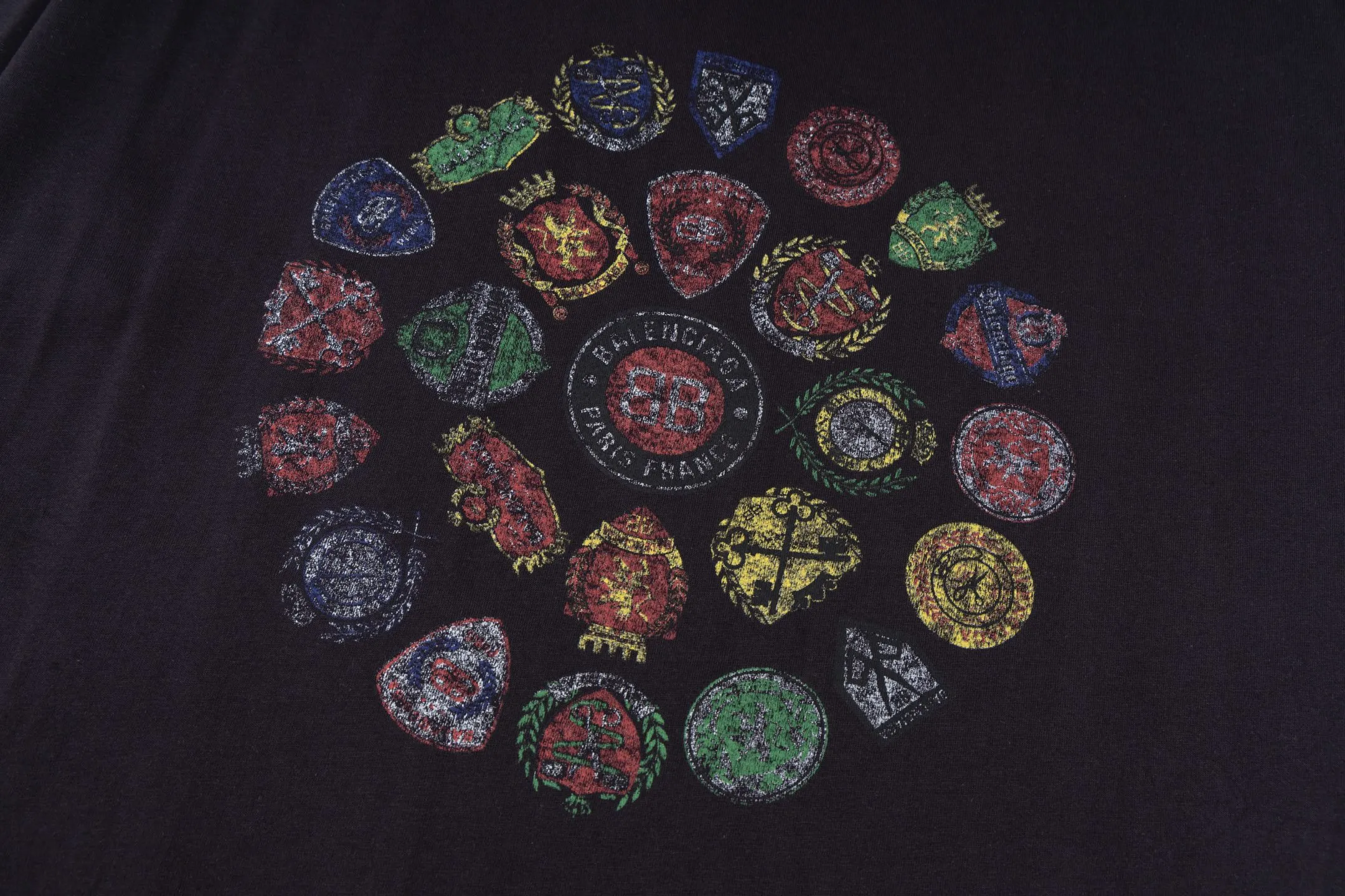 🅿️290 [Exclusive supply] BLCG 25FW badge printed short sleeves (black) The fabric is made of 24S 185g double yarn special textile compact cotton, and the rib is made of 32S 340g double yarn stretch rib. The structure of pure cotton fabric is plain weave. The surface of the fabric is smooth and delicate, and the texture is tight. It has good moisture absorption, breathability and comfort, and can keep you dry and comfortable. Due to its tight spinning process, it also has good wrinkle resistance and durability, making it suitable for long-term wear or use. The multi-layer superposition process of dark flower paste dots uses precision screen technology to cover the fabric with translucent printing paste through multiple layered printing. Each layer is laminated and fused with micron-level tolerances. Through subtle changes in the thickness and density of the slurry, an invisible pattern with a transition between dark and light is formed on the surface of the fabric. This technology replaces color contrast with physical accumulation, and uses the diffuse reflection of light on concave and convex surfaces to present a looming light and shadow relief effect, creating a high-end print with both visual haziness and tactile three-dimensionality, which perfectly fits the low-key and luxurious design aesthetics. Size:XS-S-M-L