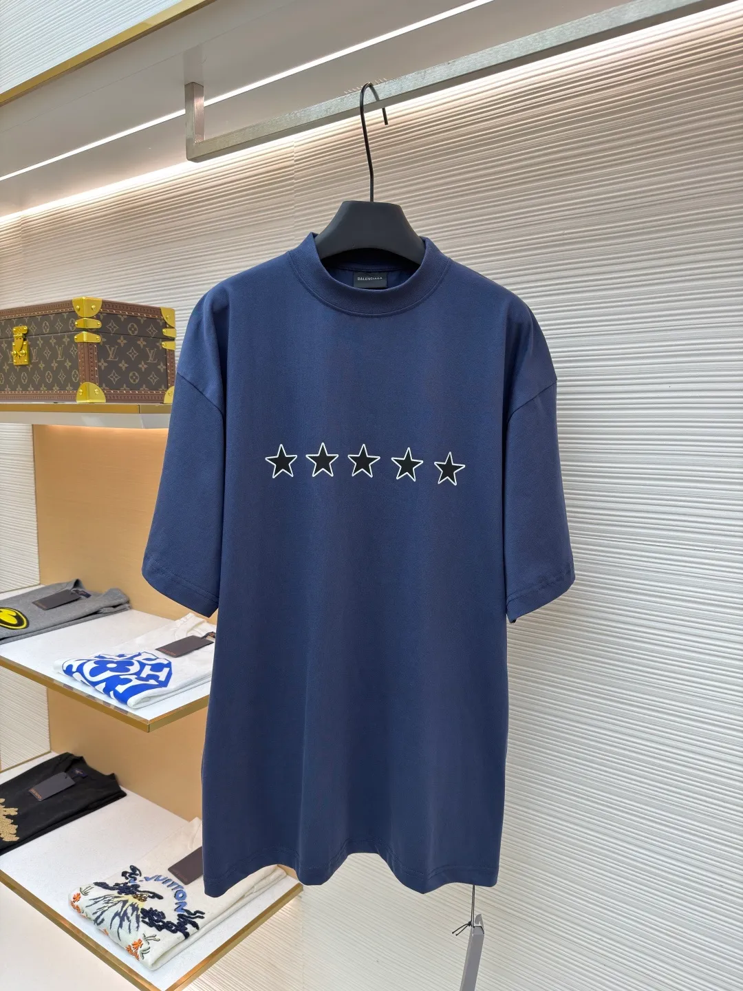 Balenciaga star embroidered short sleeves [comes with marker] ●Item number: 1682275-A20 ●Material: combed cotton fabric ●Technology: embroidery printing ●Color: blue ●Version: loose fit ●Weight: about 355 grams ●Size: XS-S-M-L ●Description: This navy blue short-sleeved T-shirt is made of high-density piqué mesh cotton fabric. The fabric has been custom-woven and dyed. The navy blue tone is uniform and not easy to fade. The breathable structure formed by the piqué texture makes the wearer more refreshing. At the same time, the fabric has excellent stiffness and can support the loose shoulder silhouette. The five-star pattern on the chest adopts double-track offset printing + inlay embroidery process. First, the outline of the stars is outlined with high-temperature embossing using matte silicone material. The thickness of the silicone layer is controlled at 0.3mm to ensure softness and no irritation to the skin. White embroidery thread is then used to fill in inlay along the edge of the silicone to give the star pattern a three-dimensional relief texture. The stitch density of each star reaches 12 stitches/cm, and the pattern alignment error does not exceed 0.1cm. The neckline is designed with a small stand-up collar, which is woven with ribs of the same fabric. It is not easy to loose after high-temperature pre-shrinking treatment. The side seams are spliced ​​with a seamless buried clip process to reduce friction when wearing. The overall process takes into account the texture and wearing comfort. The overall wiring is straight and delicate, the fabric is comfortable and soft, and the color is consistent without color difference. It can be matched with the same style to create a fashionable look and control various occasions. Customized accessories, complete with three standards, same style for men and women!