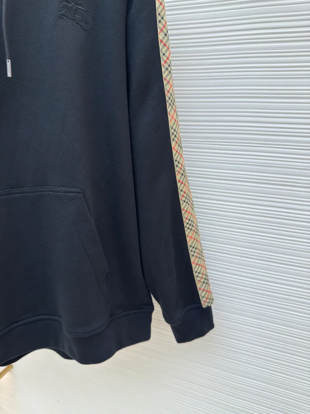 BURBERRY Ribbon trim hooded pullover sweatshirt ●Authentic product: Purchased and developed by 6239 ●Item number: 1680511-B15 ●Fabric: single-sided fish scale fabric ●Technology: selvedge production ●Version: fitted version ●Weight: about 895 grams ●Size: S-M-L-XL ●Description: A single-sided fish-scale cloth fabric woven with cotton as the base. The front is a smooth knitted surface, and the skin-contacting surface is formed into three-dimensional terry by the floating thread knitting technology of the knitting machine, which increases the fluffiness and has a delicate touch. The terry structure absorbs a large amount of water and evaporates quickly, so it is not easy to loosen and deform after repeated washing. By actively interfering with the shrinkage potential of cotton fibers, the fabric is able to transition from changeable to stable, improving dimensional stability while being less prone to deformation and wrinkles. The monochrome flat embroidery on the chest uses the high-precision calculation system of the computer embroidery machine to control the coordinated operation of the machine head, needle bar, and thread spool. The fabric frame moves accurately in the horizontal and vertical directions to form a stitch track. The upper and lower thread tensions are adjusted to ensure that the stitches are smooth and free of floating threads, forming a fine pattern with an error of ±0.1mm. The overall wiring is straight and delicate, the fabric is comfortable and soft, and the color is consistent without color difference. It can be matched with the same style to create a fashionable look and control various occasions. Customized accessories, complete with three standards, same style for men and women!