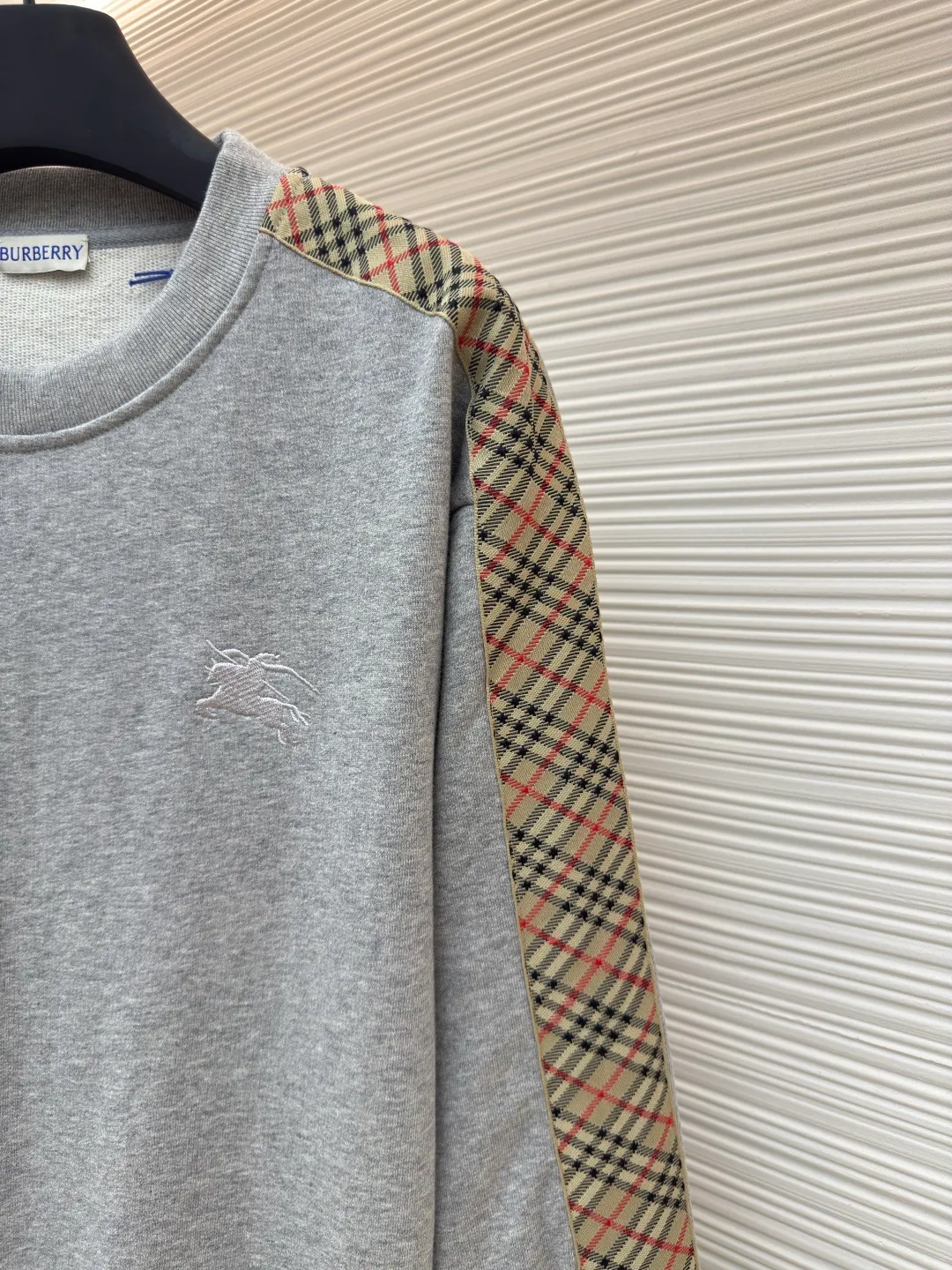 BURBERRY webbing trim round neck sweatshirt ●Authentic product: purchased and developed by 6155 ●Item number: 1680512-A85 ●Fabric: single-sided fish scale fabric ●Technology: selvedge production ●Version: fitted version ●Weight: about 645 grams ●Size: S-M-L-XL ●Description: A single-sided fish-scale cloth fabric woven with cotton as the base. The front is a smooth knitted surface, and the skin-contacting surface is formed into three-dimensional terry by the floating thread knitting technology of the knitting machine, which increases the fluffiness and has a delicate touch. The terry structure absorbs a large amount of water and evaporates quickly, so it is not easy to loosen and deform after repeated washing. By actively interfering with the shrinkage potential of cotton fibers, the fabric is able to transition from changeable to stable, improving dimensional stability while being less prone to deformation and wrinkles. The monochrome flat embroidery on the chest uses the high-precision calculation system of the computer embroidery machine to control the coordinated operation of the machine head, needle bar, and thread spool. The fabric frame moves accurately in the horizontal and vertical directions to form a stitch track. The upper and lower thread tensions are adjusted to ensure that the stitches are smooth and free of floating threads, forming a fine pattern with an error of ±0.1mm. The overall wiring is straight and delicate, the fabric is comfortable and soft, and the color is consistent without color difference. It can be matched with the same style to create a fashionable look and control various occasions. Customized accessories, complete with three standards, same style for men and women!
