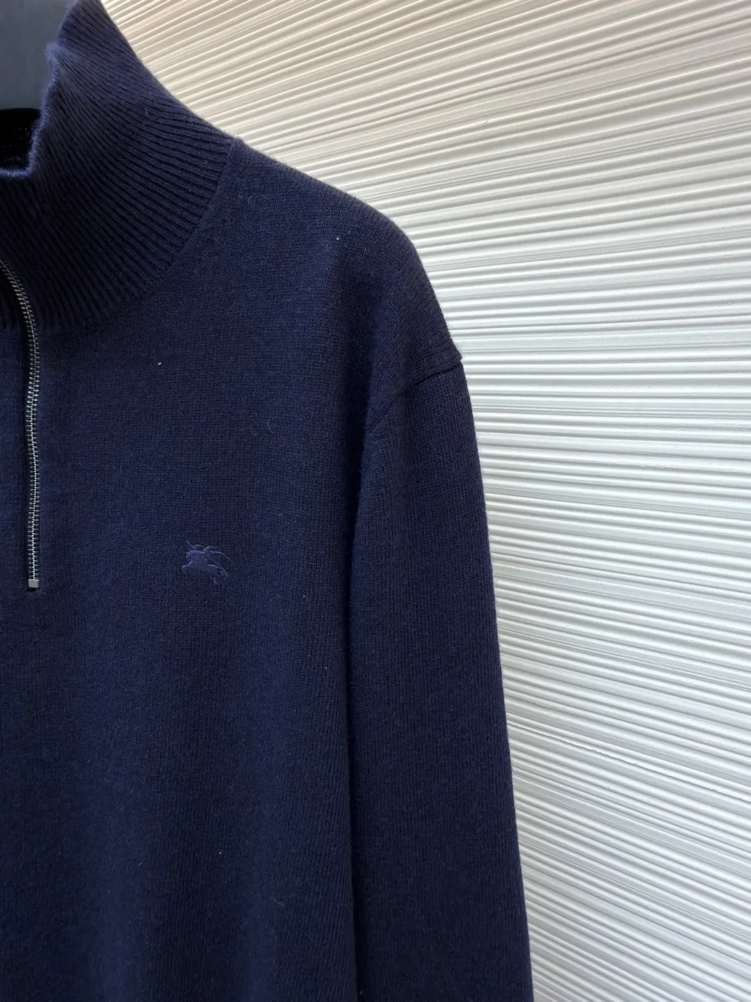 Burberry embroidered half-zip turtleneck sweater ●Original version: Purchased and developed by 4472 ●Item number: 1681783-B25 ●Material: wool blended fabric ●Technology: knitted production ●Color: navy ●Version: Fitted version ●Weight: about 545 grams ●Size: S-M-L-XL ●Description: Cashmere is used as the main body to dominate the feel, warmth and lightness of the fabric, while providing an unparalleled wearing experience. A small amount of polyamide and Lycra are added to enhance the overall durability and pilling resistance. An invisible support network is woven into the soft cashmere, and it also has a certain amount of elasticity to better fit the curves of the human body and allow it to be retracted and retracted freely. Due to the characteristics of the sweater fabric, it is stretched just right when stretching the frame, and then a hot-melt liner is used under the wool fabric piece to provide it with a certain temporary stable support to prevent it from shrinking after removal, causing pattern distortion, wrinkles and stitch dents. The high-precision calculation program system of the computer embroidery machine controls the movement of the embroidery frame in the X/Y direction, while the needle shuttles up and down, embroidering according to the set path, automatically completing thread trimming, thread jumping and other actions to form a stitch track, automatically adjusting the upper and lower thread tension to ensure that the stitches are smooth and free of floating threads, forming a war horse pattern with an error of ±0.1mm. Add detergent and preliminarily rinse the bulk goods at a water temperature of about 35 degrees to remove impurities during the production process, and then use protease to gently digest the hairiness on the surface to reduce the tendency of pilling from the root, improve the hand feel, retain softness, and eliminate irritation. After the final dehydration and drying process, the overall wiring is straight and delicate, the fabric is comfortable and soft, and the color is consistent without color difference. It can be matched with the same style to create a fashionable look and control various occasions. Customized accessories, complete with three standards, same style for men and women!