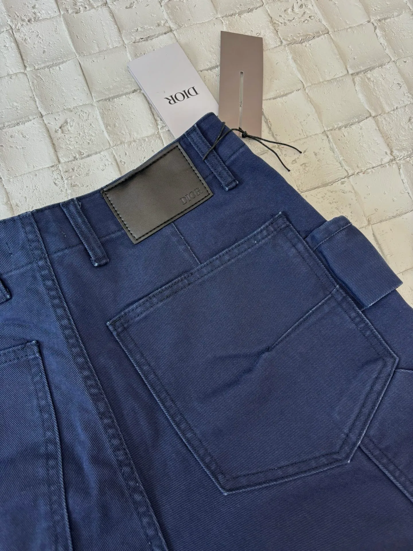 🅿️550 Dio*/Dior 25Fw new workwear blue logging French work pants. Customized twill denim (fixed dyed blue-purple) twill weaving structure. The yarn is customized using long-staple cotton + trace elastic fiber (≤3%) blend. Through the ring spinning + siro spinning composite process, the yarn has high strength and delicate surface. Pre-dyed yarn, cotton yarn is first dip-dyed with indigo 6 times (3-4 times for ordinary jeans) to ensure that the core layer is dyed through. The post-finishing uses nano-scale fixatives to give the blue a deep-sea gradient effect.   The front panel is three-dimensionally spliced, and the five-piece structure of traditional overalls is disassembled into nine asymmetrical pieces. The ergonomic curves are determined through 3D laser scanning. Double-needle differential feeding is used at the seam bone (spacing 2.5mm) to ensure no cracking during stretching.    The back leather is made of calfskin from HAAS leather factory, which is vegetable tanned and hand-rubbed to give it a matte lizard texture. Environmentally friendly dyeing uses water-based dyes, and the edge of the leather label is processed with burnt edge sealing to prevent burrs.    Size: 48/50/52