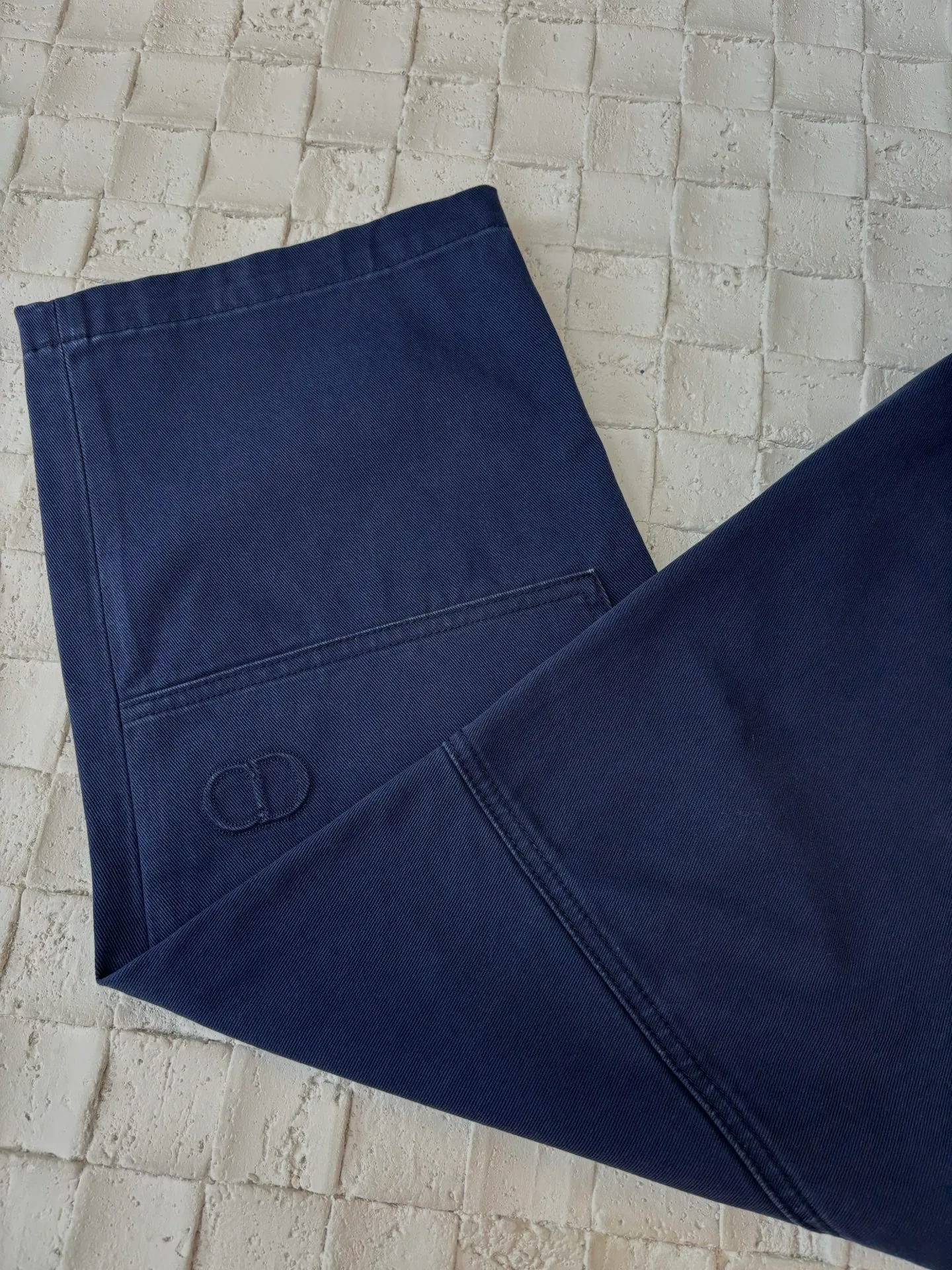 🅿️550 Dio*/Dior 25Fw new workwear blue logging French work pants. Customized twill denim (fixed dyed blue-purple) twill weaving structure. The yarn is customized using long-staple cotton + trace elastic fiber (≤3%) blend. Through the ring spinning + siro spinning composite process, the yarn has high strength and delicate surface. Pre-dyed yarn, cotton yarn is first dip-dyed with indigo 6 times (3-4 times for ordinary jeans) to ensure that the core layer is dyed through. The post-finishing uses nano-scale fixatives to give the blue a deep-sea gradient effect.   The front panel is three-dimensionally spliced, and the five-piece structure of traditional overalls is disassembled into nine asymmetrical pieces. The ergonomic curves are determined through 3D laser scanning. Double-needle differential feeding is used at the seam bone (spacing 2.5mm) to ensure no cracking during stretching.    The back leather is made of calfskin from HAAS leather factory, which is vegetable tanned and hand-rubbed to give it a matte lizard texture. Environmentally friendly dyeing uses water-based dyes, and the edge of the leather label is processed with burnt edge sealing to prevent burrs.    Size: 48/50/52