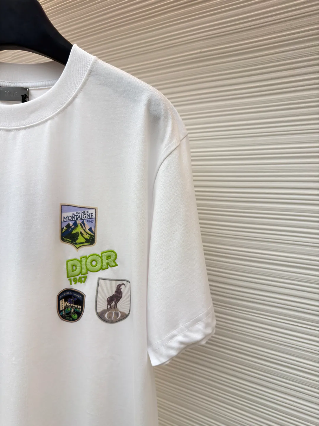 Dior Alpine Embroidery Round Neck Short Sleeve ●Original version: Purchased and developed by 7149 ●Item number: 1681102-X95 ●Fabric: plain knitted fabric ●Technology: white ink direct injection production ●Version: fitted version ●Weight: about 200 grams ●Size: S-M-L-XL ●Description: The main body is made of 24S special woven compact cotton to make plain knitted fabric, weight 180g. High-count combed cotton yarn eliminates most of the short hairiness through compact spinning process, making the yarn smoother and stronger. The woven fabric structure is extremely dense, flat and soft, with excellent anti-pilling ability and durability, while retaining the natural advantages of pure cotton, which is breathable and skin-friendly. The neckline is made of 32S 1x1 rib with a weight of 300g. The finer yarn count creates a more delicate and tight thread, which provides better elasticity and deformation resistance than ordinary ribs, ensuring that the neckline can still remain stiff after being put on and taken off many times. The printed pattern and classic logo inspired by the mountain spirit on the chest become the visual focus through the decoration combined with multiple techniques. The printed pattern elements use digital white ink direct injection technology, which presents bright, opaque white and color patterns on dark fabrics with clear edges and a smooth touch. The classic logo is completed with fluorescent green contrasting letters in the form of patches, which are then precisely sewn onto the fabric using appliqué technology. This process restores the three-dimensionality, color saturation and detail accuracy of the pattern to the original version. With the standard round neck shape and basic color, this product has established a high degree of matching tolerance. It can be mixed and matched with daily jeans or shorts, catering to the pursuit of functionality, comfort and details. The neckline has a rounded arc, suitable for various face shapes and body shapes; the sleeves are moderate and end just above the elbow, showing a smart and neat image. The slim-fitting cut shows off the wearer's body curves without sacrificing comfort. The collar, cuffs, hem and other parts are all sewn with fine double-needle stitching. The overall wiring is straight and delicate, the fabric is comfortable and soft, and the color is consistent without color difference. It can be matched with the same style to create a fashionable look and control various occasions. Customized accessories, complete with three standards, same style for men and women!
