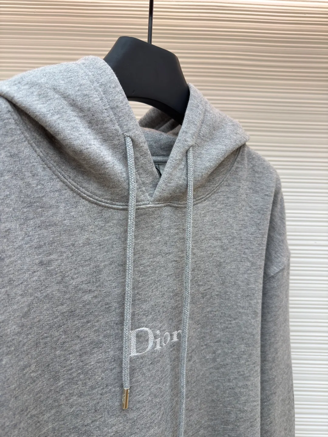 Dior classic logo embroidered hooded sweatshirt ●Item number: 1682332-A75 ●Material: cotton fabric ●Technology: embroidery production ●Color: gray ●Version: fitted version ●Weight: about 645 grams ●Size: XS-S-M-L ●Description: It adopts a fleece fabric structure of 26 counts of double yarn + 10S plush bottom, with a weight of 380g/㎡, and 21 counts of 1x1 ribs with a weight of 470g/㎡. It is used for the cuffs and hem. Its extremely high weight ensures the ultimate thickness, stiffness and deformation resistance of these closing parts, forming a unified and strong outline with the body. The fabric is a heavyweight and high-quality sweatshirt fabric. The 26-count double yarn forms a smooth, delicate and strong outer surface of the fabric, ensuring good color fastness and appearance. The 10S plush base undergoes a precise fleece or brushing process to form a layer of rich, dense and uniform fluff on the inside of the fabric. This makes the sweatshirt have a crisp and skeletal feel on the outside and an extremely soft and warm feel on the inside. White tone twill needle embroidery process. Needle embroidery is a straight line embroidery with stitches closely connected and evenly arranged. It is often used to outline clear and sharp outlines. This stitch is used to embroider a diagonal stripe pattern with a certain angle and width. Use white embroidery thread to follow the preset diagonal trajectory and perform precise embroidery with high-density stitches. On the high-weight fabric base, simple, exquisite and three-dimensional line decoration is created. The contrast between white and fabric color is sharp, and the slightly convex texture brought by the embroidery adds a visual and tactile layer, effectively enhancing the exquisite style of the basic sweatshirt. The overall wiring is straight and delicate, the fabric is comfortable and soft, and the color is consistent without color difference. It can be matched with the same style to create a fashionable look and control various occasions. Customized accessories, complete with three standards, same style for men and women!