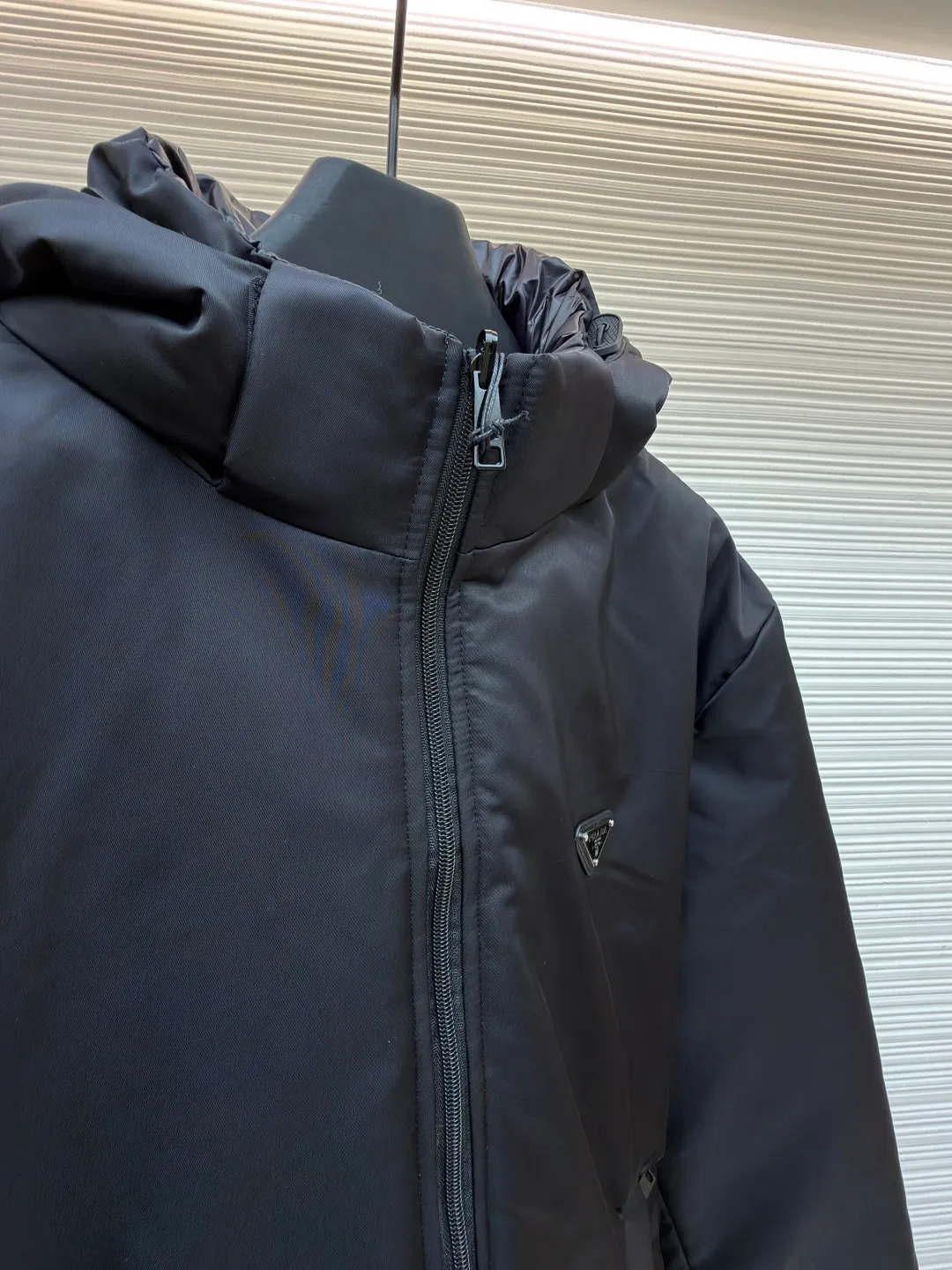 Prada mid-length nylon hooded down jacket ●Original version: purchased and developed for 15999 ●Item number: 1681587-D35 ●Fabric: white duck down fabric ●Technology: mechanical down filling ●Color: black ●Version: fitted version ●Weight: about 1155 grams ●Size: S-M-L-XL ●Description: Re-Nylon short down jacket uses environmentally friendly Re-Nylon material, the fabric density is very high It has strong tear resistance, strong stiffness and wear resistance. It is different from the Bird brand's hard shell, it is softer and has a very strong sense of functionality. Double-sided design: The biggest highlight of this down jacket is its double-sided design, which allows one piece of clothing to show two different styles and shapes, greatly increasing the diversity and fashion sense of wearing. Detachable hood: The down jacket is equipped with a detachable nylon hood, which users can easily remove or install according to weather changes or personal preferences, which is both practical and convenient. The details are exquisitely processed: the zipper design is simple and elegant, easy to operate; the closing design of the cuffs and hem effectively prevents the intrusion of cold wind, improving the warmth and comfort of wearing. All the hangtags, wash marks, air holes, snap buttons, and chest labels are all custom-made using original one-to-one molds.  The overall wiring is straight and delicate, the fabric is comfortable and soft, and the color is consistent without color difference. It can be matched with the same style to create a fashionable look and control various occasions. Customized accessories, complete with three standards, same style for men and women!