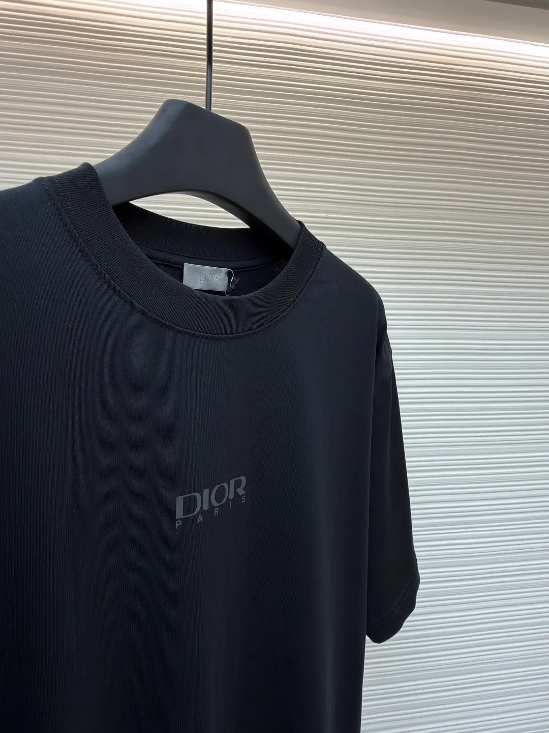 Dior Reflective Triangle Icon Round Neck Short Sleeve ●Original version: Purchased and developed by 6323 ●Item No.: 1681099-A00 ●Fabric: Jersey fabric ●Technology: Reflective lettering and embossed production ●Version: Fitted version ●Weight: about 220 grams ●Size: S-M-L-XL ●Description: The main body is made of 24S special woven compact cotton to make jersey fabric, weight 180g. High-count combed cotton yarn eliminates most of the short hairiness through compact spinning process, making the yarn smoother and stronger. The woven fabric structure is extremely dense, flat and soft, with excellent anti-pilling ability and durability, while retaining the natural advantages of pure cotton, which is breathable and skin-friendly. The neckline is made of 32S 1x1 rib with a weight of 300g. The finer yarn count creates a more delicate and tight thread, which provides better elasticity and deformation resistance than ordinary ribs, ensuring that the neckline can still remain stiff after being put on and taken off many times. The reflective engraving and embossing process is a sophisticated technology that combines safety functions with visual aesthetics. The core is to use a reflective lettering film with a built-in micro-glass bead layer. First, a high-precision laser cutting machine is used to engrave the outline according to the designed fonts and patterns to ensure that the edges are clear and burr-free. The cut reflective film is accurately attached to the surface of the fabric through heat transfer printing equipment under specific temperature and pressure, so that it is firmly combined with the fabric fibers. The case is matte silver-gray under normal conditions, but when illuminated by light, the micro-glass bead layer can achieve efficient retroreflection and instantly present a striking bright effect. The finished product is washable and abrasion resistant, perfectly meeting the dual needs of sportswear for functionality and visual tension. The overall wiring is straight and delicate, the fabric is comfortable and soft, and the color is consistent without color difference. It can be matched with the same style to create a fashionable look and control various occasions. Customized accessories, complete with three standards, same style for men and women!