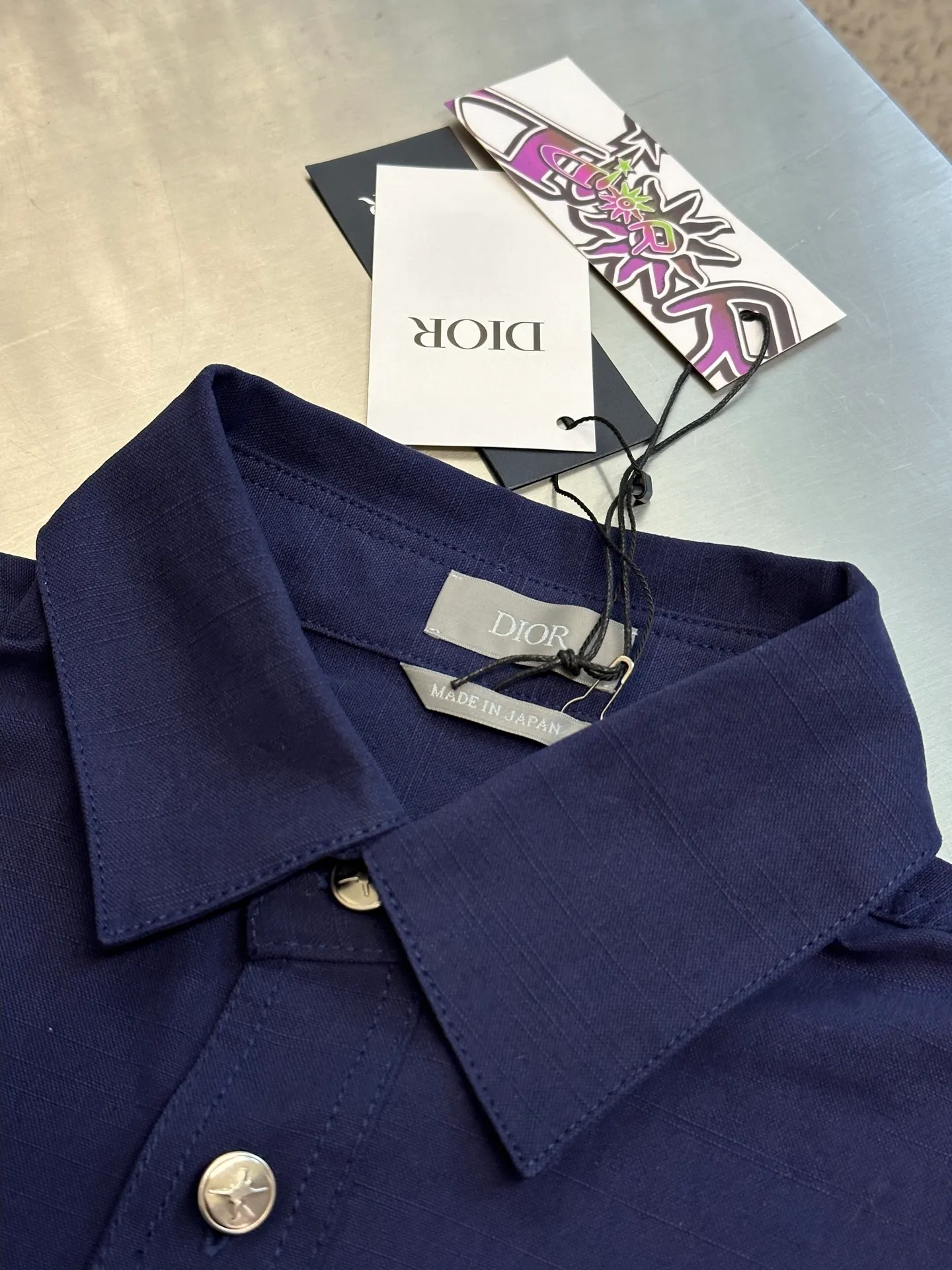 🅿️490 Dior LEWIS HAMILTON Curtain Call Shirt Crafted from blue cotton, it is decorated with patch pockets on the chest, one of which is embellished with tonal co-branded embroidery, reinterpreting the logo in a graphic style. Pair with shorts from the limited collection for a refined look.  Chambray is made of plain weave, which is characterized by interweaving yarn materials of different colors in the warp and weft. It can reflect different levels of light and shade under different light angles, and the colors are rich in changes. The cloth is light and thin in texture, smooth and soft in body, and comfortable to wear. After a specific finishing process, its elasticity and feel are further improved.  Flat stitch embroidery three-dimensional craft is a special embroidery technique that uses flat stitch to create embroidery with a three-dimensional feel. This process creates a richer three-dimensional effect and layering by precisely controlling the depth and angle of the stitches and increasing the density and length.  size:36.38.40.42