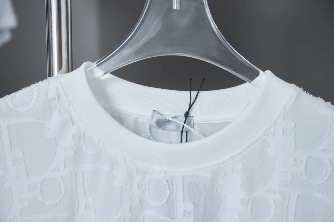 🅿️180 Dior 2025 new style embossed jacquard short-sleeved pure cotton plain fabric, woven with 32S double-strand pure cotton yarn. The 32S double-strand is twisted from two 32-count single yarns. The yarn is thicker and stronger. The fabric has high wear resistance while retaining the moisture absorption and breathability of pure cotton. The plain weave has a tight structure and a smooth surface, but it feels relatively stiff and supports the stiffness of the pattern. The jacquard pattern uses thread-cutting jacquard technology, and the full-width Oblique jacquard pattern forms a relief effect through the deep integration of full-width jacquard and shearing technology. The jacquard structure provides a three-dimensional frame, and the shearing process enhances local texture. The electronic jacquard machine is used to weave complex patterns on the entire fabric to form a three-dimensional concave and convex texture, achieving the integration of texture and pattern. The raised jacquard is cut in a directional manner to create a relief effect, enhancing tactile layering and visual contrast. Straight crew neck fit. Cut and sewn in floral position, standard H hanging fit, with shoulder-length design. The vertical version emphasizes that the width of the shoulders, waist, and hem are basically the same, and it is simple and loose. The short sleeves are tailored to fit the body of the wearer. At the same time, the neckline, cuffs and hem of the short sleeves are all designed with double lines. S M L XL