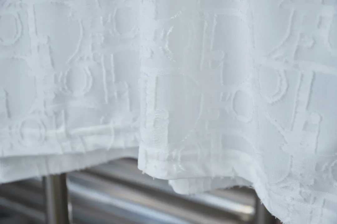 🅿️180 Dior 2025 new style embossed jacquard short-sleeved pure cotton plain fabric, woven with 32S double-strand pure cotton yarn. The 32S double-strand is twisted from two 32-count single yarns. The yarn is thicker and stronger. The fabric has high wear resistance while retaining the moisture absorption and breathability of pure cotton. The plain weave has a tight structure and a smooth surface, but it feels relatively stiff and supports the stiffness of the pattern. The jacquard pattern uses thread-cutting jacquard technology, and the full-width Oblique jacquard pattern forms a relief effect through the deep integration of full-width jacquard and shearing technology. The jacquard structure provides a three-dimensional frame, and the shearing process enhances local texture. The electronic jacquard machine is used to weave complex patterns on the entire fabric to form a three-dimensional concave and convex texture, achieving the integration of texture and pattern. The raised jacquard is cut in a directional manner to create a relief effect, enhancing tactile layering and visual contrast. Straight crew neck fit. Cut and sewn in floral position, standard H hanging fit, with shoulder-length design. The vertical version emphasizes that the width of the shoulders, waist, and hem are basically the same, and it is simple and loose. The short sleeves are tailored to fit the body of the wearer. At the same time, the neckline, cuffs and hem of the short sleeves are all designed with double lines. S M L XL