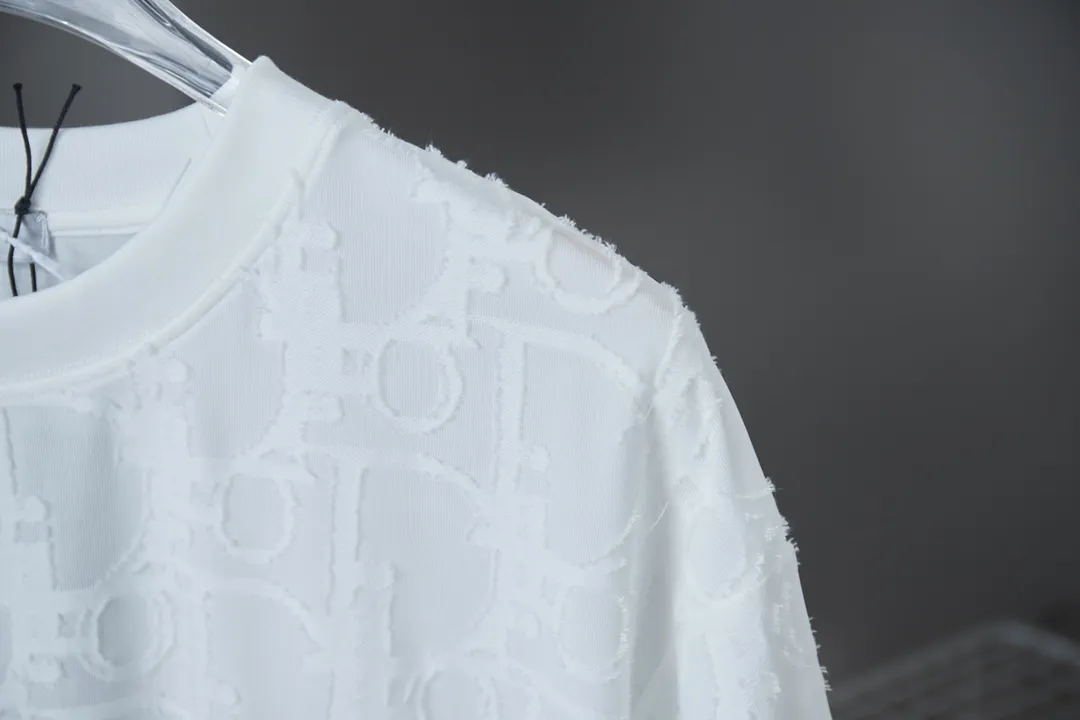 🅿️180 Dior 2025 new style embossed jacquard short-sleeved pure cotton plain fabric, woven with 32S double-strand pure cotton yarn. The 32S double-strand is twisted from two 32-count single yarns. The yarn is thicker and stronger. The fabric has high wear resistance while retaining the moisture absorption and breathability of pure cotton. The plain weave has a tight structure and a smooth surface, but it feels relatively stiff and supports the stiffness of the pattern. The jacquard pattern uses thread-cutting jacquard technology, and the full-width Oblique jacquard pattern forms a relief effect through the deep integration of full-width jacquard and shearing technology. The jacquard structure provides a three-dimensional frame, and the shearing process enhances local texture. The electronic jacquard machine is used to weave complex patterns on the entire fabric to form a three-dimensional concave and convex texture, achieving the integration of texture and pattern. The raised jacquard is cut in a directional manner to create a relief effect, enhancing tactile layering and visual contrast. Straight crew neck fit. Cut and sewn in floral position, standard H hanging fit, with shoulder-length design. The vertical version emphasizes that the width of the shoulders, waist, and hem are basically the same, and it is simple and loose. The short sleeves are tailored to fit the body of the wearer. At the same time, the neckline, cuffs and hem of the short sleeves are all designed with double lines. S M L XL
