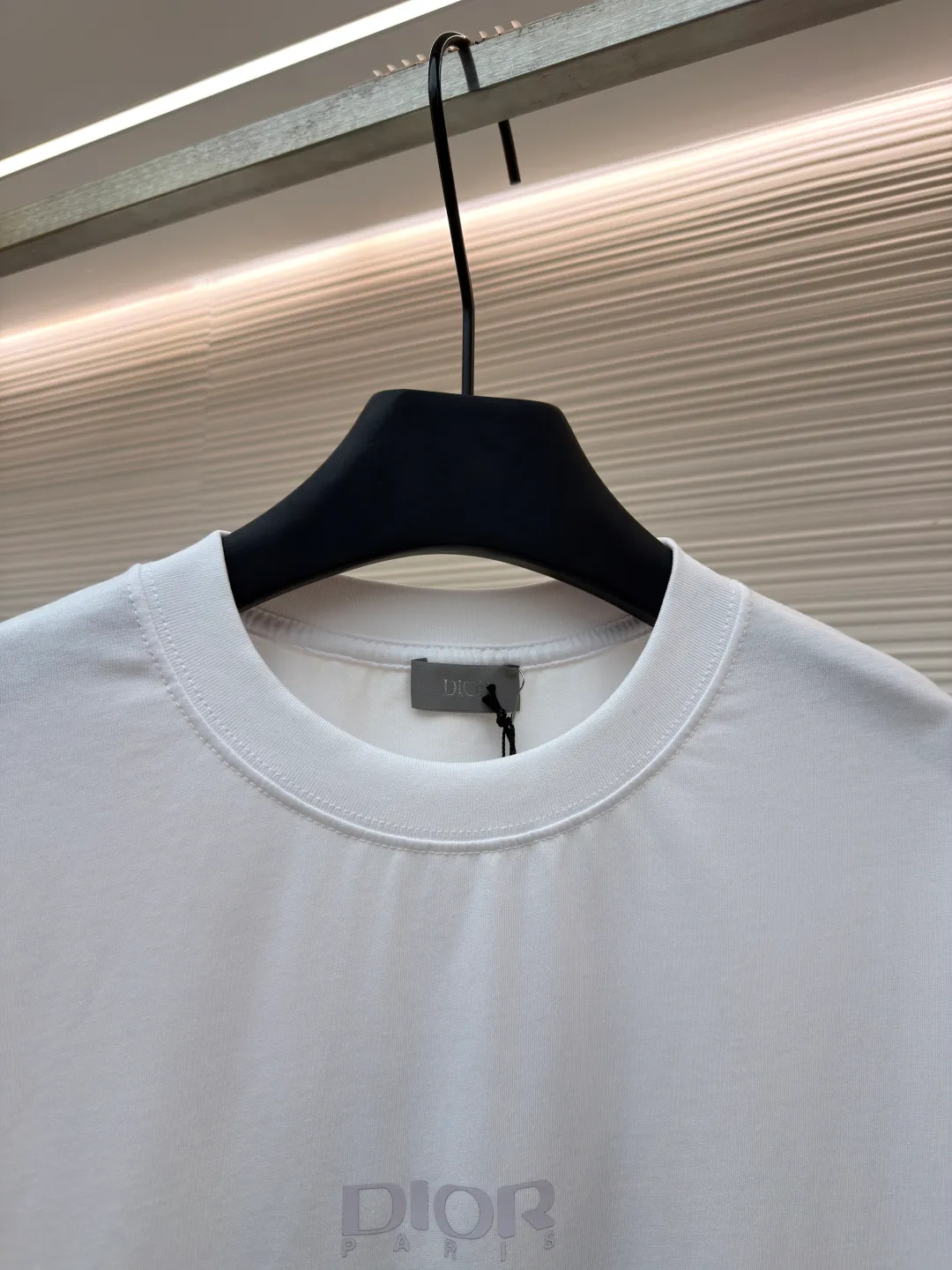 Dior Reflective Triangle Icon Round Neck Short Sleeve ●Item No.: 1681100-A00 ●Fabric: Jersey fabric ●Technology: Reflective lettering and embossed production ●Version: Fitted version ●Weight: about 205 grams ●Size: S-M-L-XL ●Description: The main body is made of 24S special woven compact cotton to make jersey fabric, weight 180g. High-count combed cotton yarn eliminates most of the short hairiness through compact spinning process, making the yarn smoother and stronger. The woven fabric structure is extremely dense, flat and soft, with excellent anti-pilling ability and durability, while retaining the natural advantages of pure cotton, which is breathable and skin-friendly. The neckline is made of 32S 1x1 rib with a weight of 300g. The finer yarn count creates a more delicate and tight thread, which provides better elasticity and deformation resistance than ordinary ribs, ensuring that the neckline can still remain stiff after being put on and taken off many times. The reflective engraving and embossing process is a sophisticated technology that combines safety functions with visual aesthetics. The core is to use a reflective lettering film with a built-in micro-glass bead layer. First, a high-precision laser cutting machine is used to engrave the outline according to the designed fonts and patterns to ensure that the edges are clear and burr-free. The cut reflective film is accurately attached to the surface of the fabric through heat transfer printing equipment under specific temperature and pressure, so that it is firmly combined with the fabric fibers. The case is matte silver-gray under normal conditions, but when illuminated by light, the micro-glass bead layer can achieve efficient retroreflection and instantly present a striking bright effect. The finished product is washable and abrasion resistant, perfectly meeting the dual needs of sportswear for functionality and visual tension. The overall wiring is straight and delicate, the fabric is comfortable and soft, and the color is consistent without color difference. It can be matched with the same style to create a fashionable look and control various occasions. Customized accessories, complete with three standards, same style for men and women!