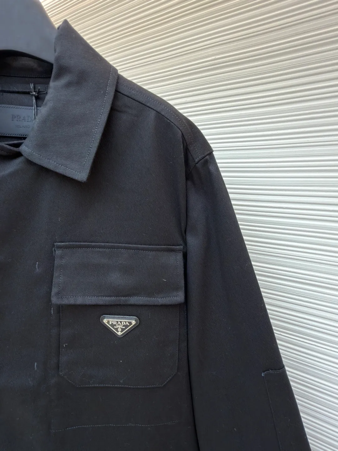 PRADA cotton work style jacket ●Original version: Purchased and developed by 14803 ●Item number: 1680864-B90 ●Fabric: nylon fabric ●Technology: Made on positioning cutting machine ●Version: fitted version ●Weight: about 760 grams ●Size: S-M-L-XL ●Description: The fabric is constructed with 45° diagonal warp and weft interweaving, and the closely arranged cotton yarns form a natural three-dimensional texture, giving it a practical base that is anti-wrinkle and wear-resistant. At the same time, the matte texture echoes the rough aesthetics of workwear style. It retains the natural skin-friendliness and sweat-absorbing ability of cotton fiber, while taking into account warmth and breathability. Utilizing the natural stiffness of the fabric, double-layer cotton yarn is used to reinforce the shoulder seams to create a sculptural wide shoulder silhouette and avoid softness and deformation. Invisible thread strips are embedded in the cuffs to ensure freedom of movement. Through low-temperature pressing and the natural hardness of twill fabric, a 30-degree stiffening angle is created to make the neckline fit the curve of the neck and improve wearing comfort. Abandoning the traditional lining, the stiffness of the fabric itself is used to shape the silhouette, reducing redundant layers while improving breathability. Hidden button closure and straight bottom hem design enhance the tough temperament and balance the loose fit, avoiding a bloated look. Symmetrical flap patch pockets enhance practicality, and the three-dimensional silhouette adds a sense of hierarchy. Tight stitching at the edges makes the bag sturdy while adding beauty. The overall wiring is straight and delicate, the fabric is comfortable and soft, and the color is consistent without color difference. It can be matched with the same style to create a fashionable look and control various occasions. Customized accessories, complete with three standards, same style for men and women!