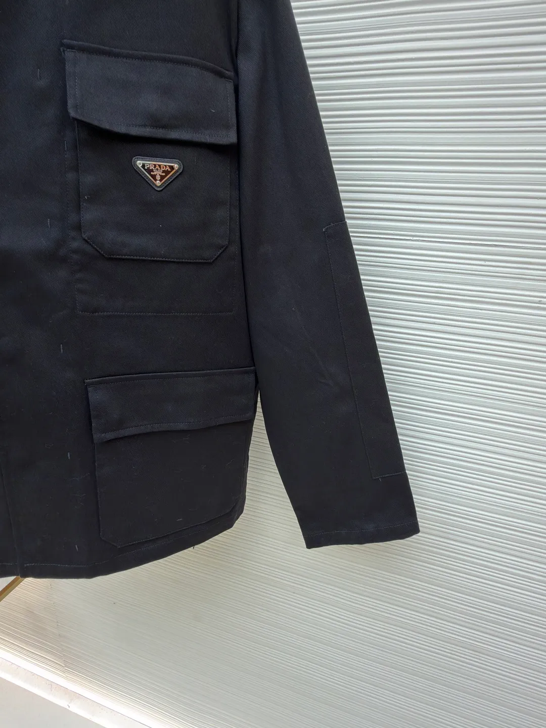 PRADA cotton work style jacket ●Original version: Purchased and developed by 14803 ●Item number: 1680864-B90 ●Fabric: nylon fabric ●Technology: Made on positioning cutting machine ●Version: fitted version ●Weight: about 760 grams ●Size: S-M-L-XL ●Description: The fabric is constructed with 45° diagonal warp and weft interweaving, and the closely arranged cotton yarns form a natural three-dimensional texture, giving it a practical base that is anti-wrinkle and wear-resistant. At the same time, the matte texture echoes the rough aesthetics of workwear style. It retains the natural skin-friendliness and sweat-absorbing ability of cotton fiber, while taking into account warmth and breathability. Utilizing the natural stiffness of the fabric, double-layer cotton yarn is used to reinforce the shoulder seams to create a sculptural wide shoulder silhouette and avoid softness and deformation. Invisible thread strips are embedded in the cuffs to ensure freedom of movement. Through low-temperature pressing and the natural hardness of twill fabric, a 30-degree stiffening angle is created to make the neckline fit the curve of the neck and improve wearing comfort. Abandoning the traditional lining, the stiffness of the fabric itself is used to shape the silhouette, reducing redundant layers while improving breathability. Hidden button closure and straight bottom hem design enhance the tough temperament and balance the loose fit, avoiding a bloated look. Symmetrical flap patch pockets enhance practicality, and the three-dimensional silhouette adds a sense of hierarchy. Tight stitching at the edges makes the bag sturdy while adding beauty. The overall wiring is straight and delicate, the fabric is comfortable and soft, and the color is consistent without color difference. It can be matched with the same style to create a fashionable look and control various occasions. Customized accessories, complete with three standards, same style for men and women!