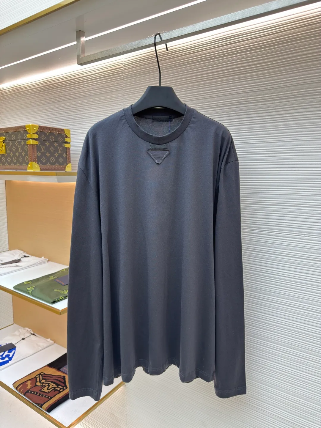 Prada Pencil Gray Long Sleeve ●Original version: Purchased and developed by 8934 ●Item number: 1680720-A05 ●Fabric: combed plain weave fabric ●Technology: Laser burning ●Version: fitted version ●Weight: about 240 grams ●Size: S-M-L-XL ●Description: Custom-woven 50S 190G combed plain weave fabric, non-market general gray fabric, needs to be fully customized from yarn ratio and loom parameters. Short fiber impurities are removed through the combing process to ensure that the yarn is longer and more uniform, and the fabric surface is smooth and hairless.  Specially dyed pencil gray, the color is adjusted individually instead of using a standard color card. Multiple proofing is required to match the low saturation gray tone specified by Prada. Chest triangle laser burnt embroidery shaping: Laser burnt: high-precision laser engraving, carbonizing the fabric surface to form a gradient etching texture, and the edges need to be manually adjusted to avoid scorch marks.  Composite embroidery: superimpose embroidery on the basis of burnt flowers. The stitch density needs to be aligned with the burnt flowers pattern to prevent fabric deformation.  Three-dimensional shaping: Use high-temperature pressing or resin coating to maintain the relief of the triangular structure and avoid collapse after washing. The overall wiring is straight and delicate, the fabric is comfortable and soft, and the color is consistent without color difference. It can be matched with the same style to create a fashionable look and control various occasions. Customized accessories, complete with three standards, same style for men and women!