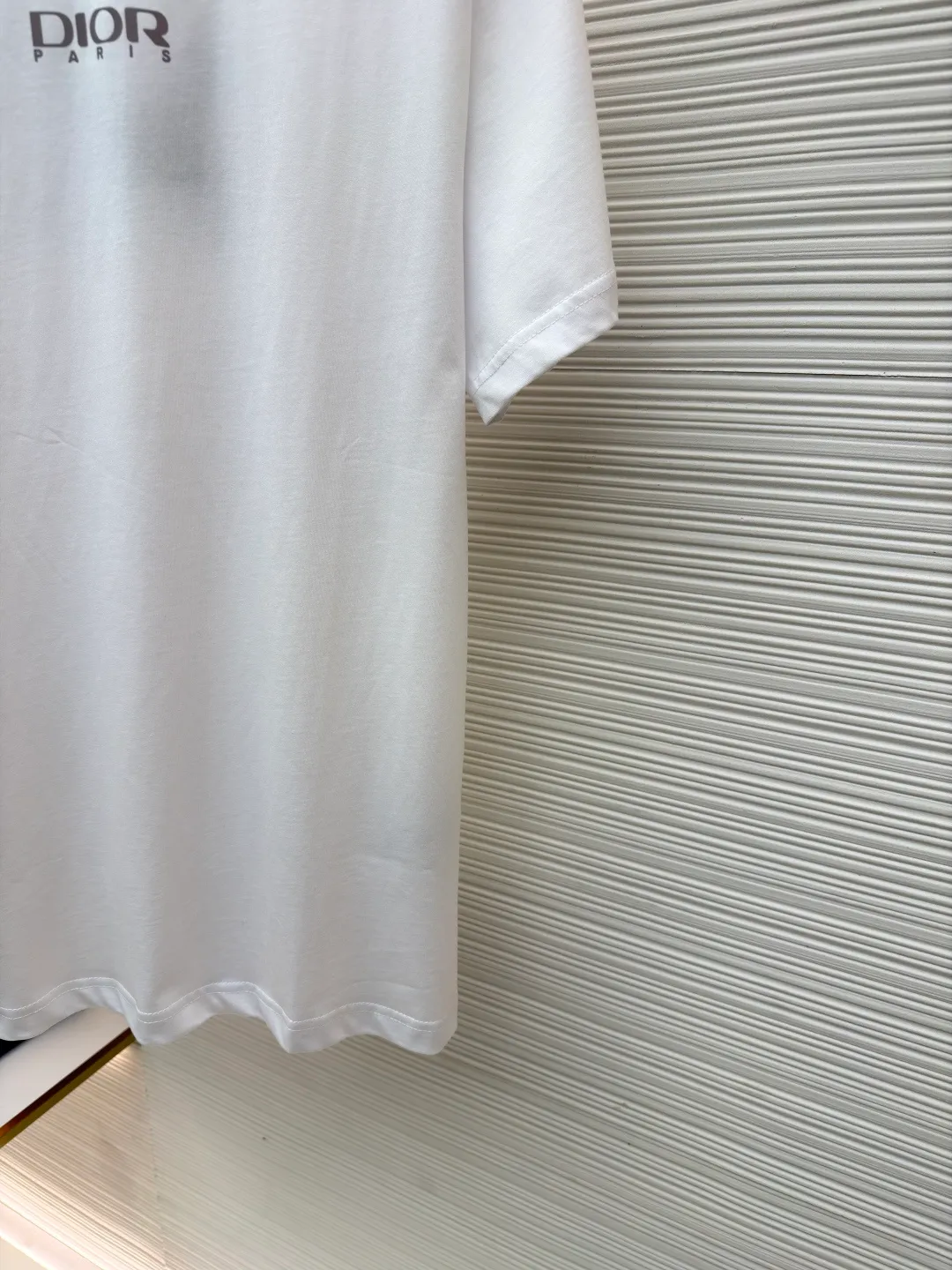 Dior Reflective Triangle Icon Round Neck Short Sleeve ●Item No.: 1681100-A00 ●Fabric: Jersey fabric ●Technology: Reflective lettering and embossed production ●Version: Fitted version ●Weight: about 205 grams ●Size: S-M-L-XL ●Description: The main body is made of 24S special woven compact cotton to make jersey fabric, weight 180g. High-count combed cotton yarn eliminates most of the short hairiness through compact spinning process, making the yarn smoother and stronger. The woven fabric structure is extremely dense, flat and soft, with excellent anti-pilling ability and durability, while retaining the natural advantages of pure cotton, which is breathable and skin-friendly. The neckline is made of 32S 1x1 rib with a weight of 300g. The finer yarn count creates a more delicate and tight thread, which provides better elasticity and deformation resistance than ordinary ribs, ensuring that the neckline can still remain stiff after being put on and taken off many times. The reflective engraving and embossing process is a sophisticated technology that combines safety functions with visual aesthetics. The core is to use a reflective lettering film with a built-in micro-glass bead layer. First, a high-precision laser cutting machine is used to engrave the outline according to the designed fonts and patterns to ensure that the edges are clear and burr-free. The cut reflective film is accurately attached to the surface of the fabric through heat transfer printing equipment under specific temperature and pressure, so that it is firmly combined with the fabric fibers. The case is matte silver-gray under normal conditions, but when illuminated by light, the micro-glass bead layer can achieve efficient retroreflection and instantly present a striking bright effect. The finished product is washable and abrasion resistant, perfectly meeting the dual needs of sportswear for functionality and visual tension. The overall wiring is straight and delicate, the fabric is comfortable and soft, and the color is consistent without color difference. It can be matched with the same style to create a fashionable look and control various occasions. Customized accessories, complete with three standards, same style for men and women!