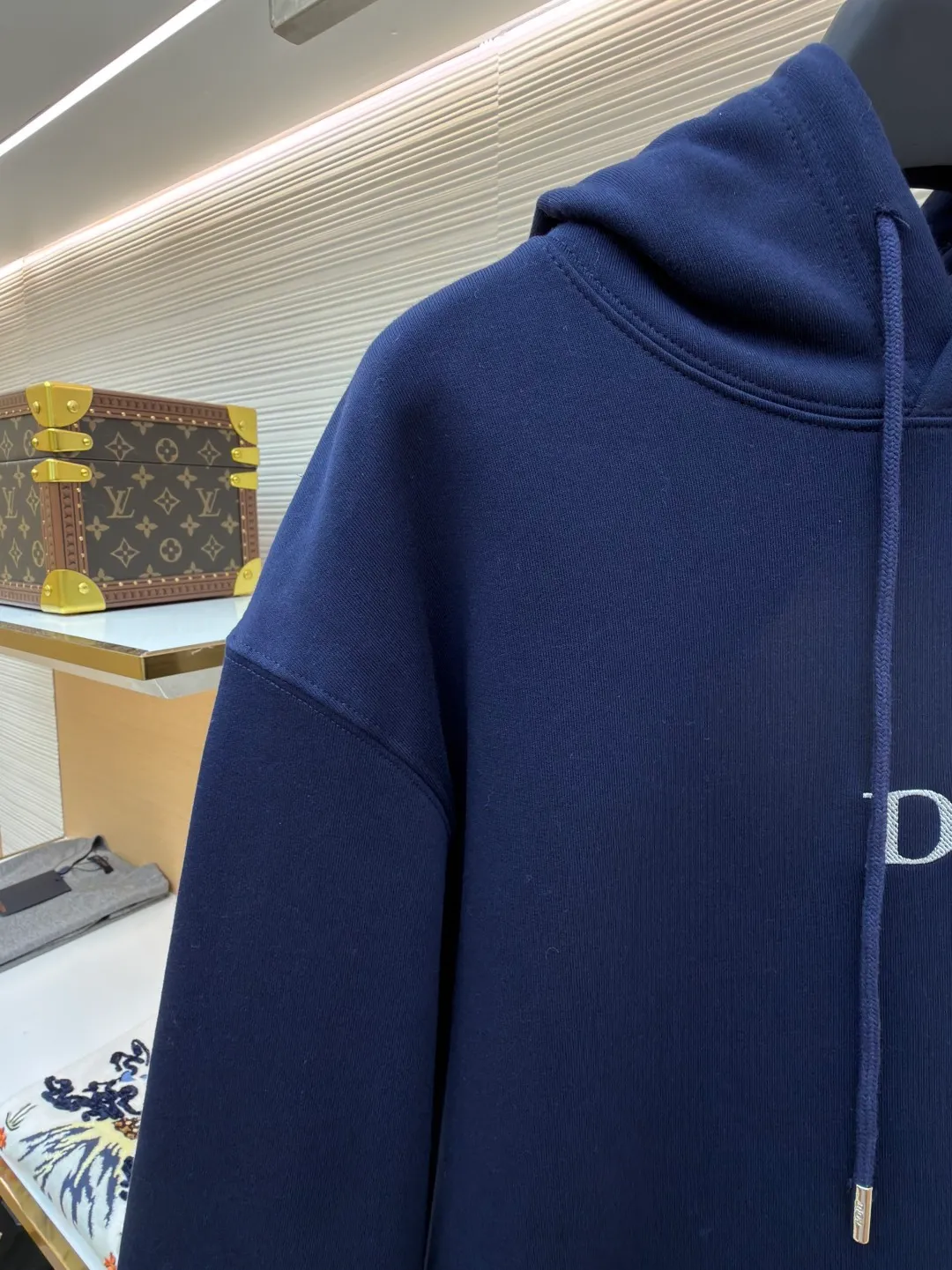 Dior classic logo embroidered hooded sweatshirt ●Item number: 1682333-A75 ●Material: cotton fabric ●Technology: embroidery production ●Color: navy blue ●Version: fitted version ●Weight: about 730 grams ●Size: XS-S-M-L ●Description: It adopts a fleece fabric structure of 26 counts of double yarn + 10S plush bottom, with a weight of 380g/㎡, and 21 counts of 1x1 ribs with a weight of 470g/㎡. It is used for the cuffs and hem. Its extremely high weight ensures the ultimate thickness, stiffness and deformation resistance of these closing parts, forming a unified and strong outline with the body. The fabric is a heavyweight and high-quality sweatshirt fabric. The 26-count double yarn forms a smooth, delicate and strong outer surface of the fabric, ensuring good color fastness and appearance. The 10S plush base undergoes a precise fleece or brushing process to form a layer of rich, dense and uniform fluff on the inside of the fabric. This makes the sweatshirt have a crisp and skeletal feel on the outside and an extremely soft and warm feel on the inside. White tone twill needle embroidery process. Needle embroidery is a straight line embroidery with stitches closely connected and evenly arranged. It is often used to outline clear and sharp outlines. This stitch is used to embroider a diagonal stripe pattern with a certain angle and width. Use white embroidery thread to follow the preset diagonal trajectory and perform precise embroidery with high-density stitches. On the high-weight fabric base, simple, exquisite and three-dimensional line decoration is created. The contrast between white and fabric color is sharp, and the slightly convex texture brought by the embroidery adds a visual and tactile layer, effectively enhancing the exquisite style of the basic sweatshirt. The overall wiring is straight and delicate, the fabric is comfortable and soft, and the color is consistent without color difference. It can be matched with the same style to create a fashionable look and control various occasions. Customized accessories, complete with three standards, same style for men and women!