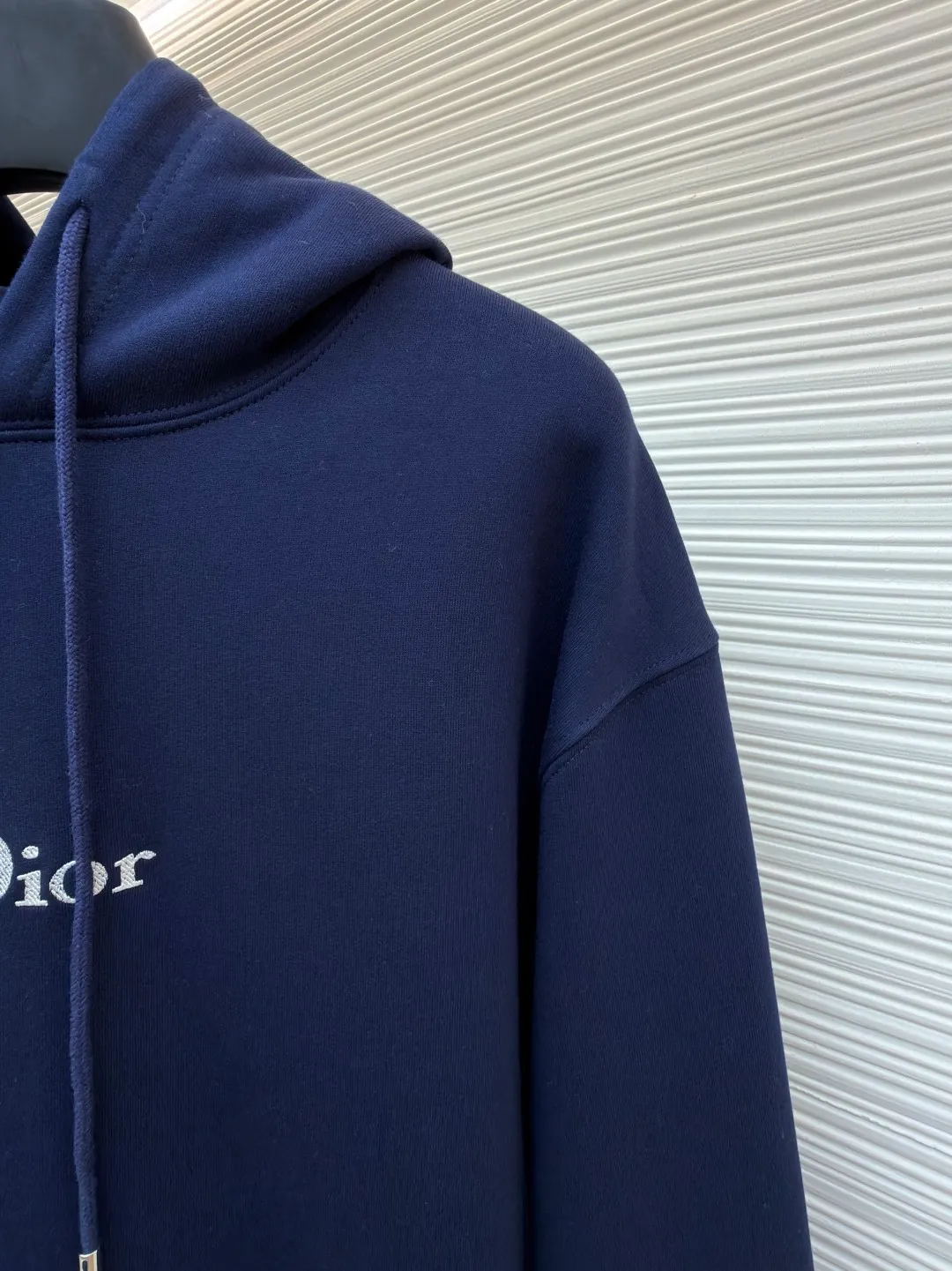 Dior classic logo embroidered hooded sweatshirt ●Item number: 1682333-A75 ●Material: cotton fabric ●Technology: embroidery production ●Color: navy blue ●Version: fitted version ●Weight: about 730 grams ●Size: XS-S-M-L ●Description: It adopts a fleece fabric structure of 26 counts of double yarn + 10S plush bottom, with a weight of 380g/㎡, and 21 counts of 1x1 ribs with a weight of 470g/㎡. It is used for the cuffs and hem. Its extremely high weight ensures the ultimate thickness, stiffness and deformation resistance of these closing parts, forming a unified and strong outline with the body. The fabric is a heavyweight and high-quality sweatshirt fabric. The 26-count double yarn forms a smooth, delicate and strong outer surface of the fabric, ensuring good color fastness and appearance. The 10S plush base undergoes a precise fleece or brushing process to form a layer of rich, dense and uniform fluff on the inside of the fabric. This makes the sweatshirt have a crisp and skeletal feel on the outside and an extremely soft and warm feel on the inside. White tone twill needle embroidery process. Needle embroidery is a straight line embroidery with stitches closely connected and evenly arranged. It is often used to outline clear and sharp outlines. This stitch is used to embroider a diagonal stripe pattern with a certain angle and width. Use white embroidery thread to follow the preset diagonal trajectory and perform precise embroidery with high-density stitches. On the high-weight fabric base, simple, exquisite and three-dimensional line decoration is created. The contrast between white and fabric color is sharp, and the slightly convex texture brought by the embroidery adds a visual and tactile layer, effectively enhancing the exquisite style of the basic sweatshirt. The overall wiring is straight and delicate, the fabric is comfortable and soft, and the color is consistent without color difference. It can be matched with the same style to create a fashionable look and control various occasions. Customized accessories, complete with three standards, same style for men and women!