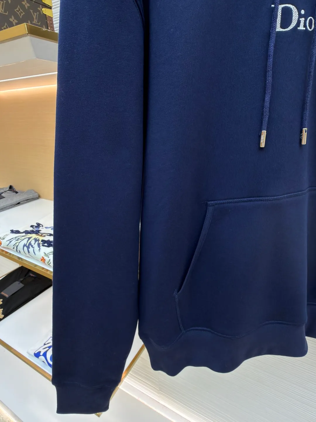 Dior classic logo embroidered hooded sweatshirt ●Item number: 1682333-A75 ●Material: cotton fabric ●Technology: embroidery production ●Color: navy blue ●Version: fitted version ●Weight: about 730 grams ●Size: XS-S-M-L ●Description: It adopts a fleece fabric structure of 26 counts of double yarn + 10S plush bottom, with a weight of 380g/㎡, and 21 counts of 1x1 ribs with a weight of 470g/㎡. It is used for the cuffs and hem. Its extremely high weight ensures the ultimate thickness, stiffness and deformation resistance of these closing parts, forming a unified and strong outline with the body. The fabric is a heavyweight and high-quality sweatshirt fabric. The 26-count double yarn forms a smooth, delicate and strong outer surface of the fabric, ensuring good color fastness and appearance. The 10S plush base undergoes a precise fleece or brushing process to form a layer of rich, dense and uniform fluff on the inside of the fabric. This makes the sweatshirt have a crisp and skeletal feel on the outside and an extremely soft and warm feel on the inside. White tone twill needle embroidery process. Needle embroidery is a straight line embroidery with stitches closely connected and evenly arranged. It is often used to outline clear and sharp outlines. This stitch is used to embroider a diagonal stripe pattern with a certain angle and width. Use white embroidery thread to follow the preset diagonal trajectory and perform precise embroidery with high-density stitches. On the high-weight fabric base, simple, exquisite and three-dimensional line decoration is created. The contrast between white and fabric color is sharp, and the slightly convex texture brought by the embroidery adds a visual and tactile layer, effectively enhancing the exquisite style of the basic sweatshirt. The overall wiring is straight and delicate, the fabric is comfortable and soft, and the color is consistent without color difference. It can be matched with the same style to create a fashionable look and control various occasions. Customized accessories, complete with three standards, same style for men and women!