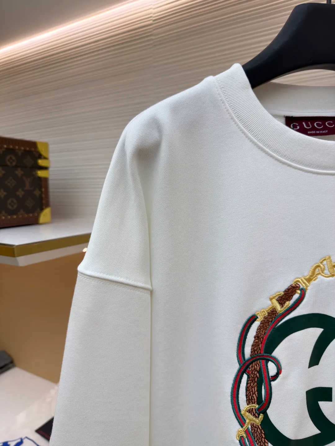Gucci Bridle Web Round Neck Sweater ●Item No.: 1682279-A65 ●Material: 100% cotton ●Technology: Embroidery ●Color: White ●Version: Fitted ●Weight: about 645 grams ●Size: XS-S-M-L ●Description: This Gucci sweatshirt is made of high-weight combed cotton fabric. The fabric is tight and elastic, which can effectively maintain the stiffness and wearing comfort. The double G logo on the front adopts multi-layer embroidery technology, with gold thread to outline the outline, red and green velvet thread to fill the texture, and metallic chain stripe pattern appliqué. The stitches are fine and even, and each embroidery is precisely positioned to form a three-dimensional contrast with the fabric texture. The body is cut according to the loose shoulder design, and the shoulder line splicing adopts overlock stitching technology to reduce friction when wearing; the cuffs and hem are edged with ribs of the same color, which has long-lasting elasticity and is not easy to loosen. Sizes from XS to L are all standardized plate making, with increasing gradients in dimensions such as garment length and shoulder width. The stitching process uses a combination of flat seams and overlock seams to ensure the firmness of the garments and the exquisiteness of details. The overall craftsmanship combines the brand's iconic design with practical wearing performance. The overall wiring is straight and delicate, the fabric is comfortable and soft, and the color is consistent without color difference. It can be matched with the same style to create a fashionable look and control various occasions. Customized accessories, complete with three standards, same style for men and women!