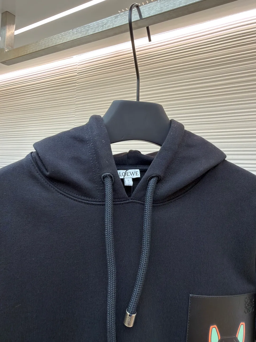 Loewe quirky kitten embossed hooded sweatshirt ●Original version: Purchased and developed by 8718 ●Item number: 1681954-A85 ●Material: pure cotton fabric ●Technology: genuine leather embossed production ●Color: black ●Version: fitted version ●Weight: about 920 grams ●Size: XS-S-M-L ●Description: This LV black hooded sweatshirt is made of 380g heavyweight fleece sweatshirt fabric. It is pre-shrunk and has a stable shape, with a fine matte texture on the surface. The hat rope is made of nylon braided rope + metal bell. The rope head is polished and rhodium-plated, with a cool texture and anti-oxidation. The chest patch pocket uses genuine leather embossing technology: the leather base is embossed with brand dark patterns, and the bag surface pattern uses multi-color silk screen printing + partial flocking. The ears, paws and other details of the animal image are raised by flocking to enhance the three-dimensional effect, and the color fastness reaches level 4 or above. The body stitching adopts double-needle overlocking technology, and the ribbing on the cuffs and hem is made of the same fabric, with an elastic rebound rate of ≥85%. The overall cutting error is controlled within 0.3cm, and the brand logo is embossed on the inside of the neckline, taking into account concealment and recognition, and balancing practicality and design. The overall wiring is straight and delicate, the fabric is comfortable and soft, and the color is consistent without color difference. It can be matched with the same style to create a fashionable look and control various occasions. Customized accessories, complete with three standards, same style for men and women!