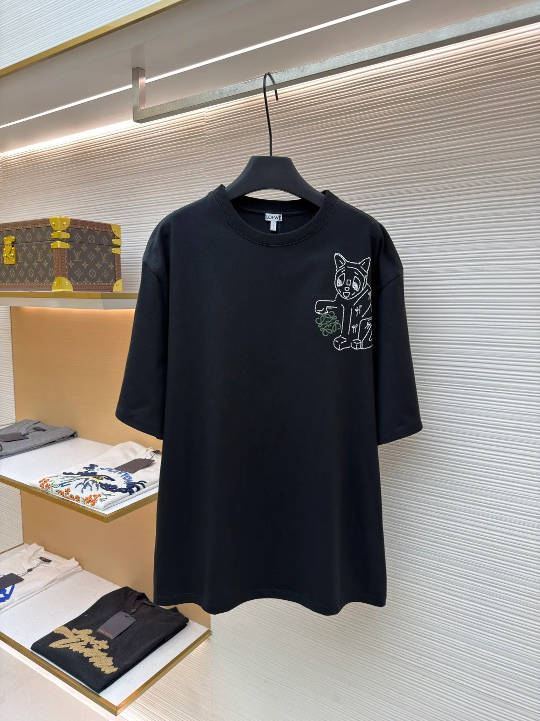 Loewe Cat Line Pattern Round Neck Short Sleeve ●Original version: Purchased and developed at 4330 ●Item number: 1681867-A00 ●Material: combed cotton fabric ●Technology: embroidery production ●Color: black ●Version: fitted version ●Weight: about 295 grams ●Size: XS-S-M-L ●Description: Made of 15S fine cotton plain fabric, 230g; with 32S double yarn thread, 300g. Plain weave fabric made from combed cotton fibers has a more orderly arrangement and higher density than ordinary cotton, so it has better texture and luster. 15S fine cotton plain fabric is a high-quality cotton fabric with the characteristics of softness, comfort, good breathability, and good durability. Anagram Embroidery Lucky Cat: The rice grain line embroidery process uses special ultra-fine embroidery thread and high-density stitching to create a pattern outline as delicate and continuous as grains. Its core feature lies in the precise arrangement of ultra-fine stitches, which require 12-15 stitches per centimeter to form full lines, and the edges present a handmade micro-waving effect. The fabric achieves a stroke-like gradient of thickness and flow. The overall pattern is light, breathable and smooth to the touch. It looks like a line outline from a distance, but the texture of interwoven fibers can be seen up close. It is especially suitable for expressing delicate details such as logo outlines and geometric borders. Anagram embroidery: Using three-dimensional embroidery technology, the logo clearly restores the spacing curve. The mercerized embroidery thread with luster is selected, combined with complex embroidery needlework and fine detail processing to create a three-dimensional relief embroidery effect. Classic trademark letter design, fine embroidery and dense stitching, clear font and strong sense of lines and three-dimensionality. The overall wiring is straight and delicate, the fabric is comfortable and soft, and the color is consistent without color difference. It can be matched with the same style to create a fashionable look and control various occasions. Customized accessories, complete with three standards, same style for men and women!